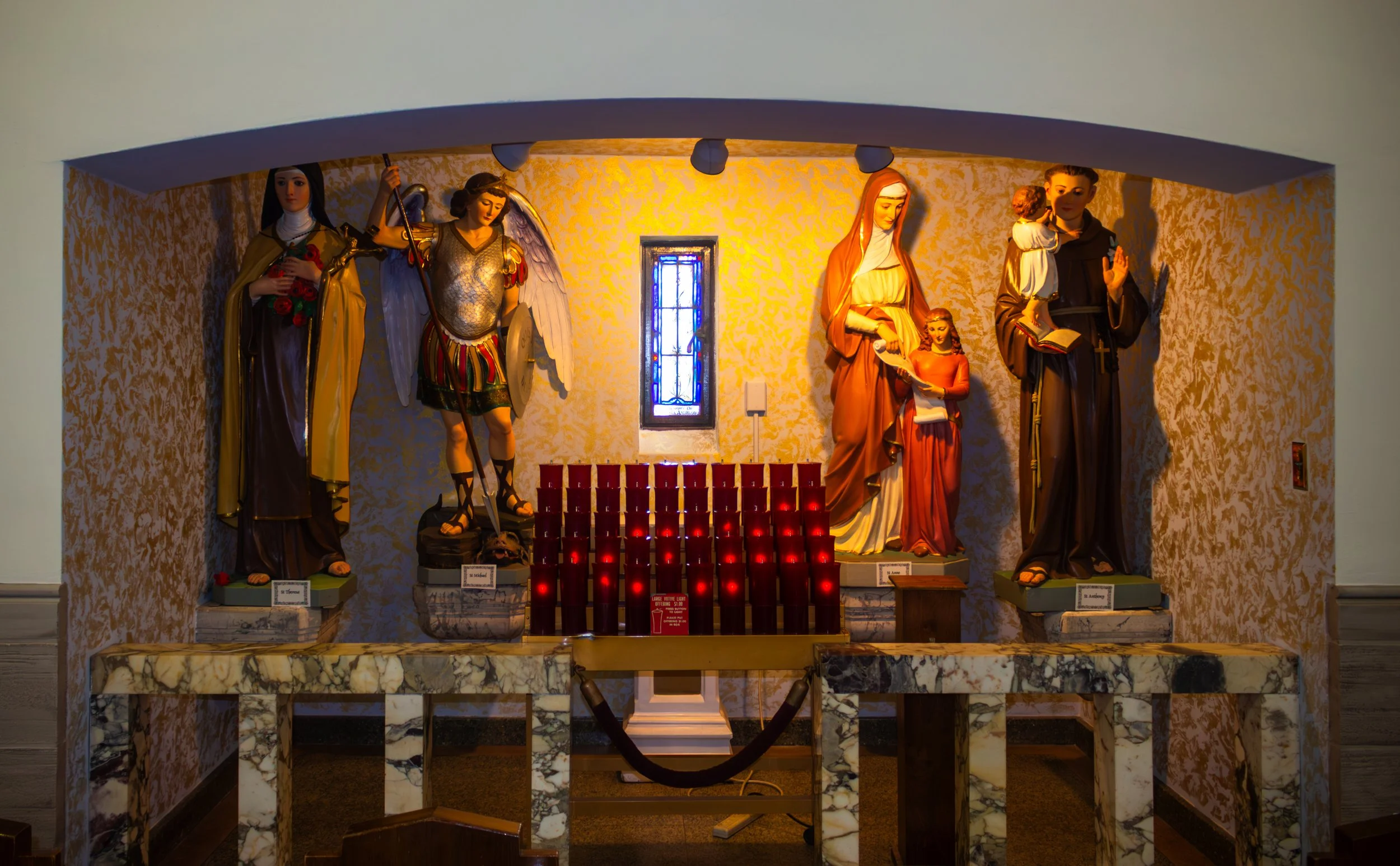 Religious altar with statues of saints, candles, and a small stained glass window