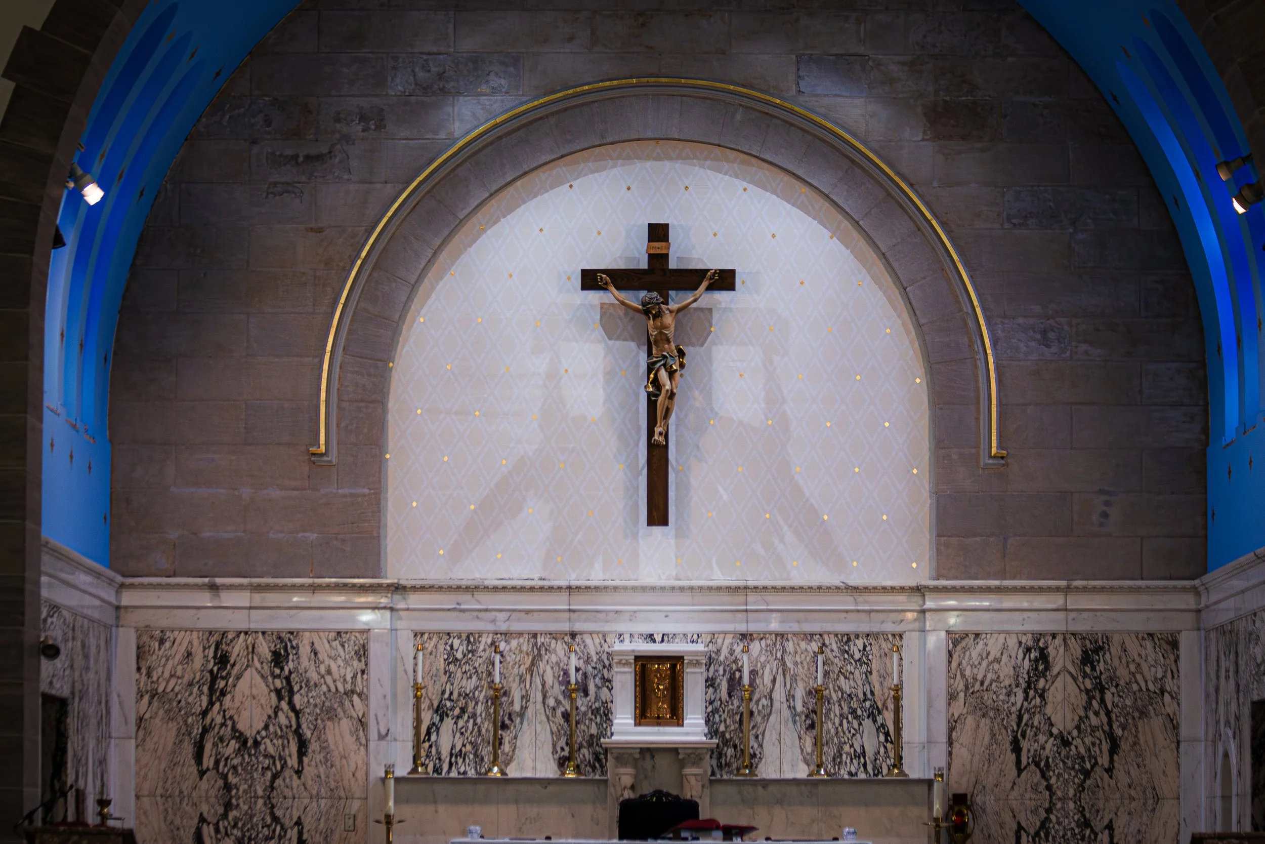 Interior view of a church altar with a crucifix on a wall, marble flooring, and a marble altar table with candles.