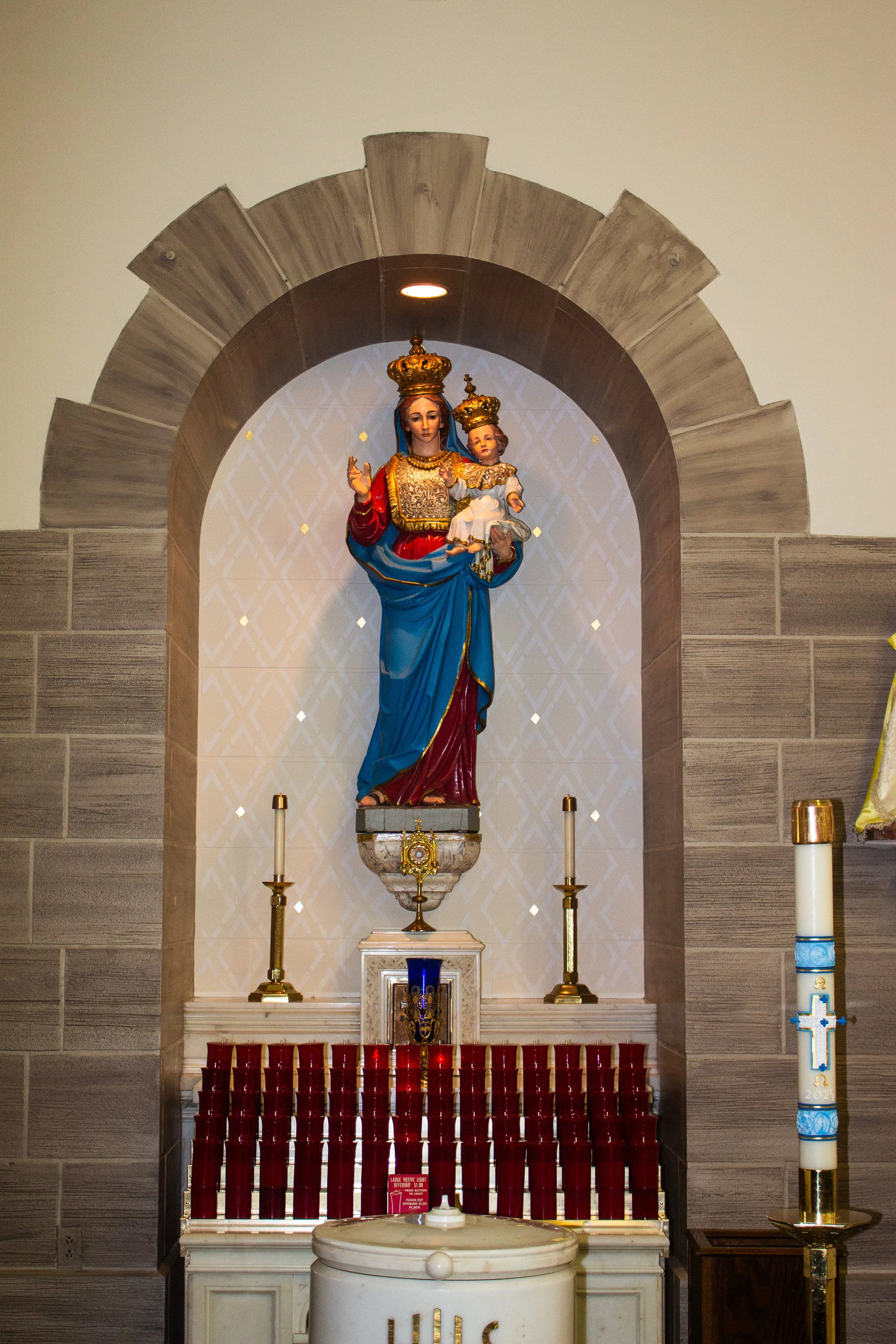 Statue of the Virgin Mary holding baby Jesus, both wearing crowns, with a religious altar including candles in front.