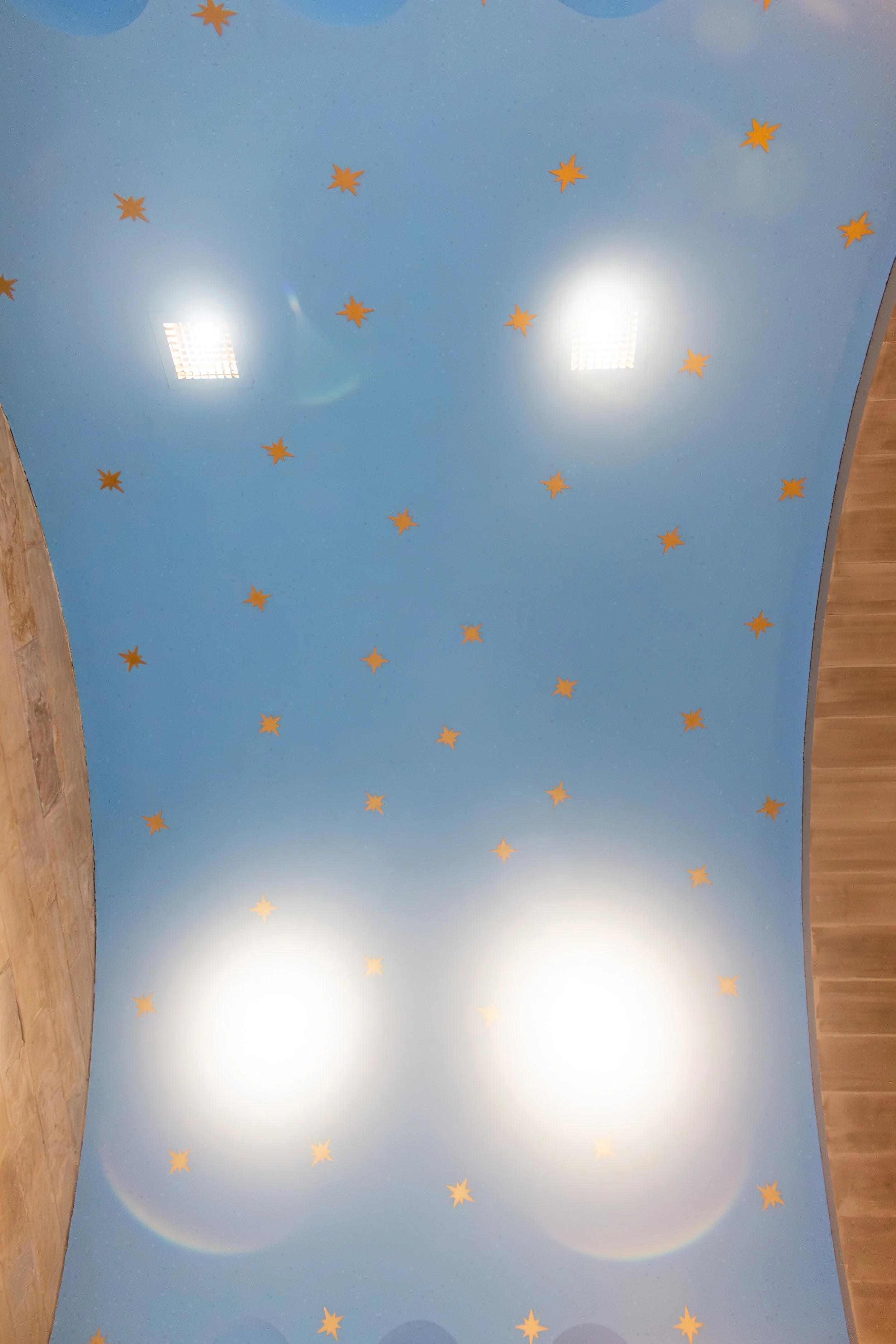 Ceiling painted light blue with small yellow star-shaped decorations evenly spaced, two bright ceiling lights, and portions of a wooden wall visible at the edges.