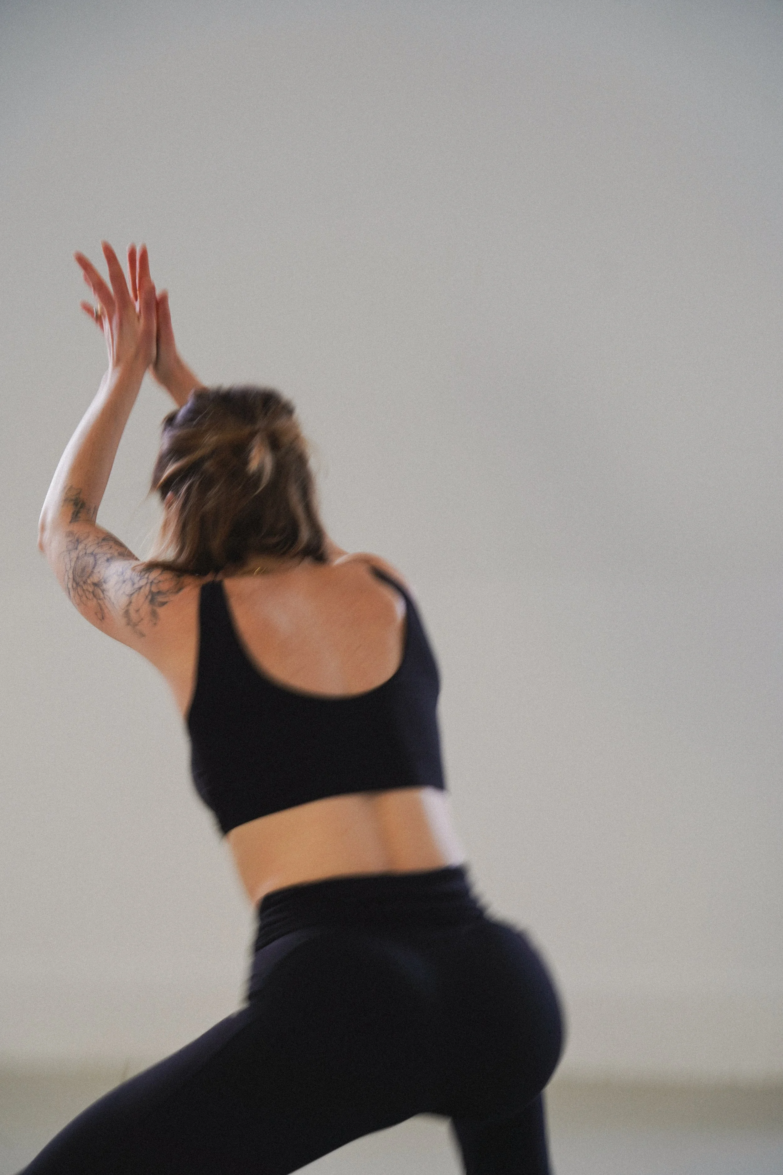 A woman dressed in black, practicing yoga or stretching against a plain background.