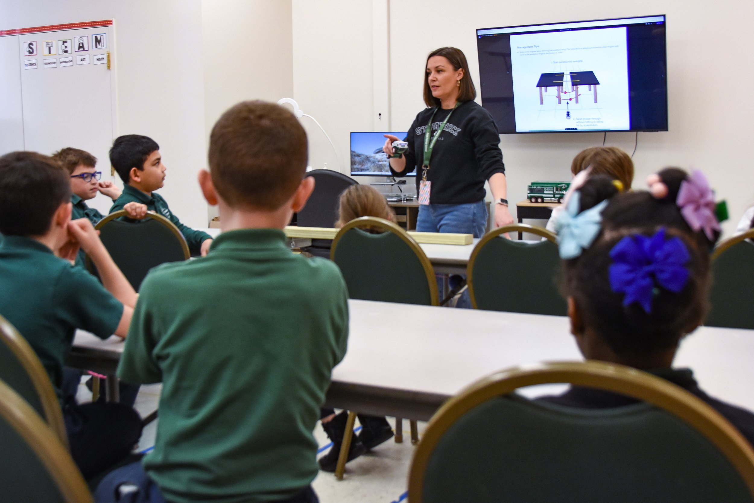 A teacher standing in front of students in a classroom, giving a presentation about management tips on a large screen