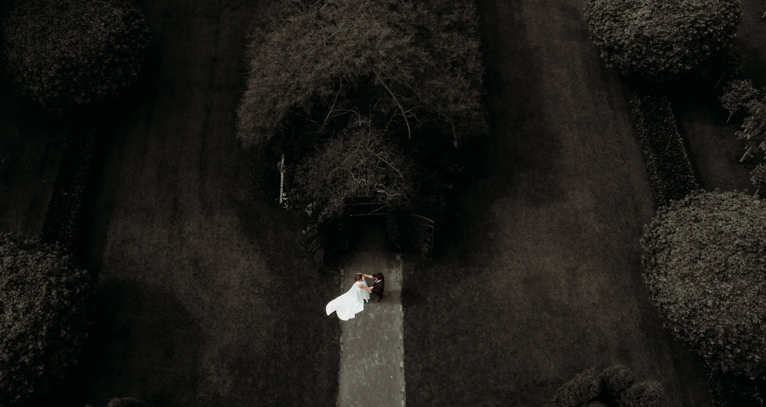 A couple holding hands and dancing on a path in a park at night, with trees and open space surrounding them. Tree church wedding venue