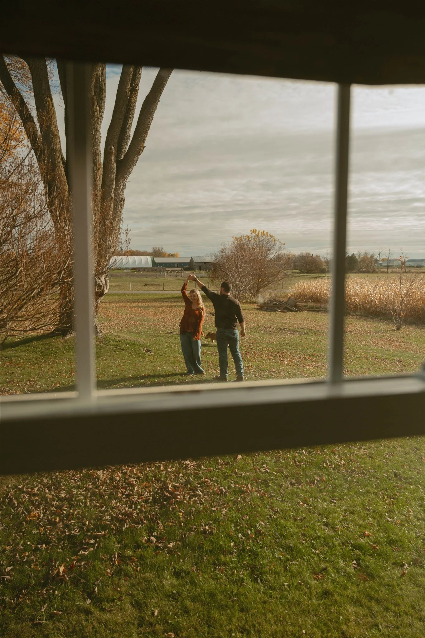 A couple dancing outdoors in a rural area viewed through a window.