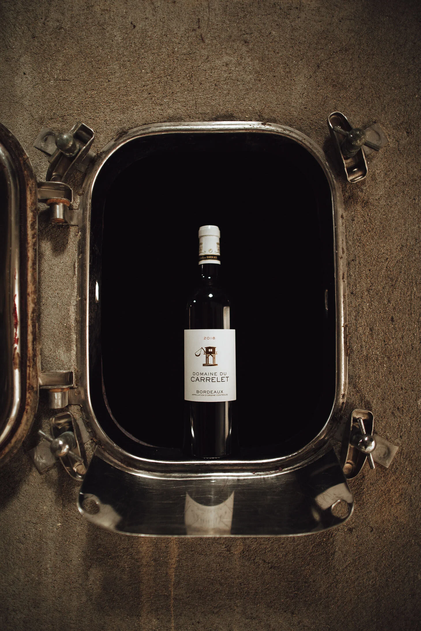 Bouteille du Domaine du Carrelet mise en valeur dans le chai, vin en AOC Bordeaux distingué par des guides et dégustateurs.