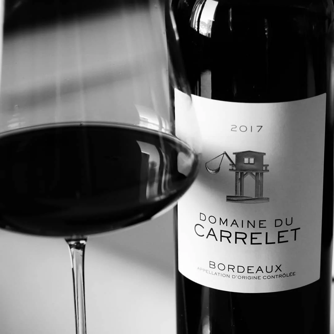 Bouteille de vin rouge du Domaine du Carrelet, micro-vignoble familial en AOC Bordeaux, avec verre de dégustation.