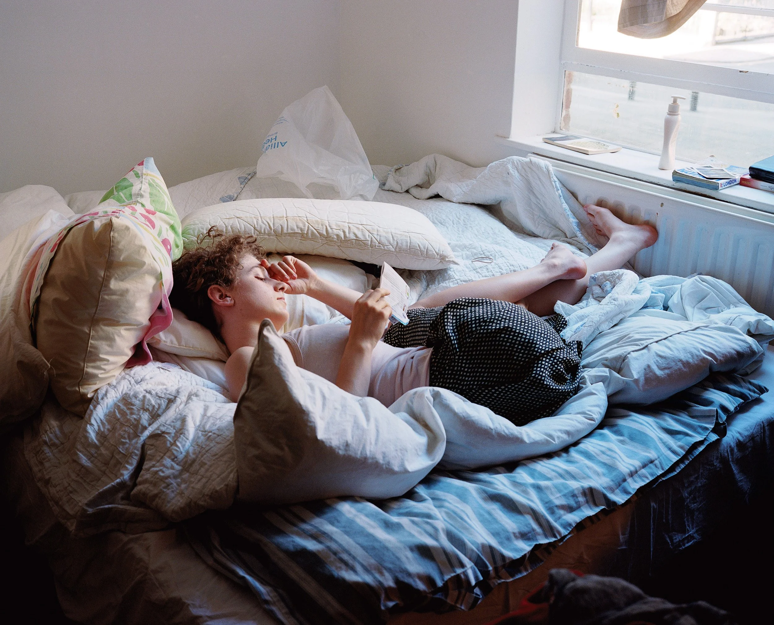 A portrait photograph of a young women on her bed in her bedroom taken by London based photographer artist Maxwell Anderson