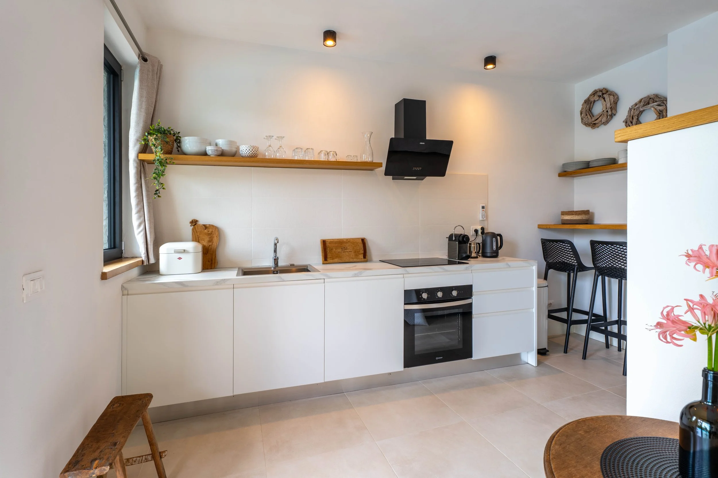Moderne keuken met witte kasten, een fornuis, een oven, een waterkoker en een koffiemachine, met houten planken en decoraties.
