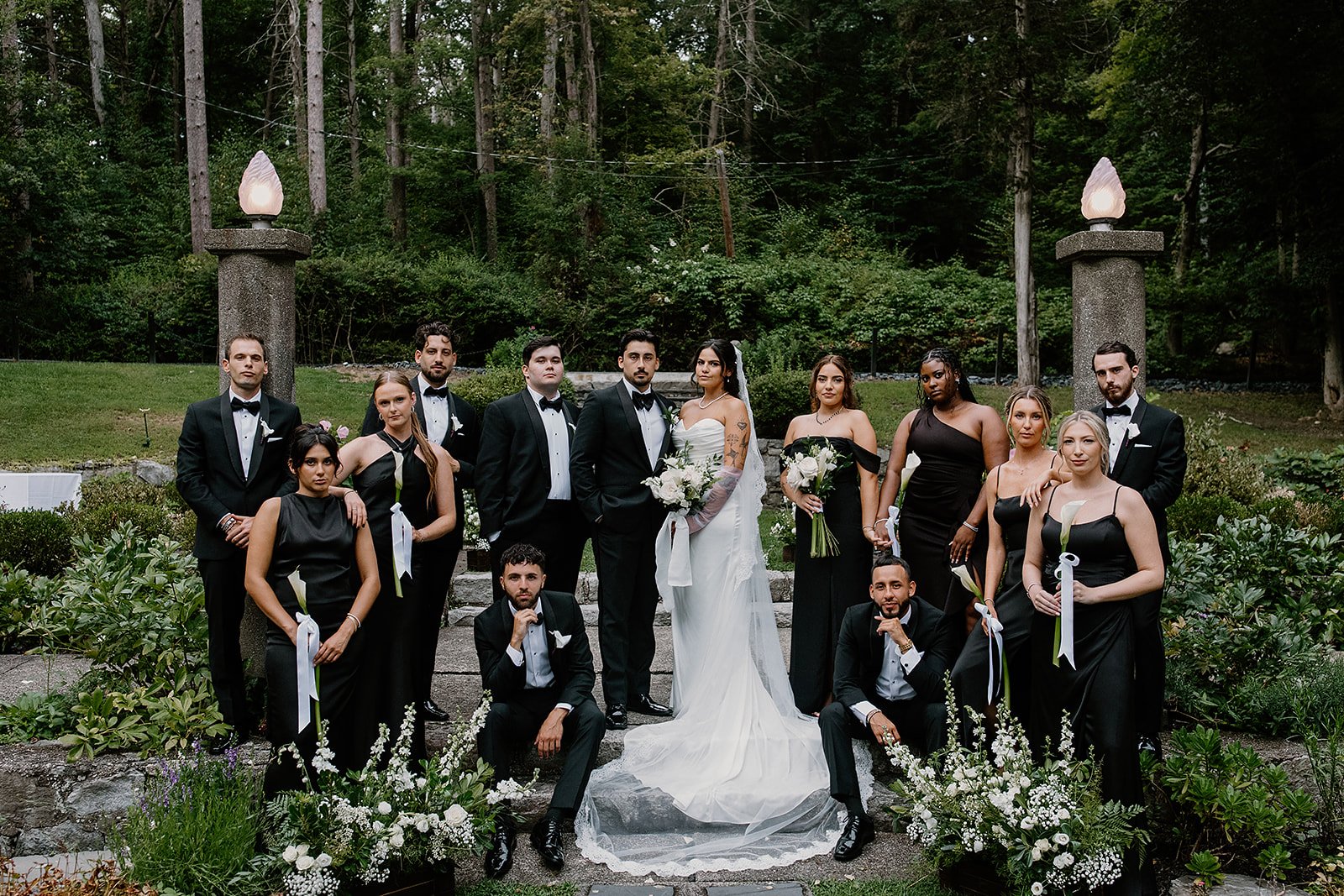 A wedding party of thirteen people pose for their final photo before enjoying cocktail hour. Wedding is at Arrow Park NY