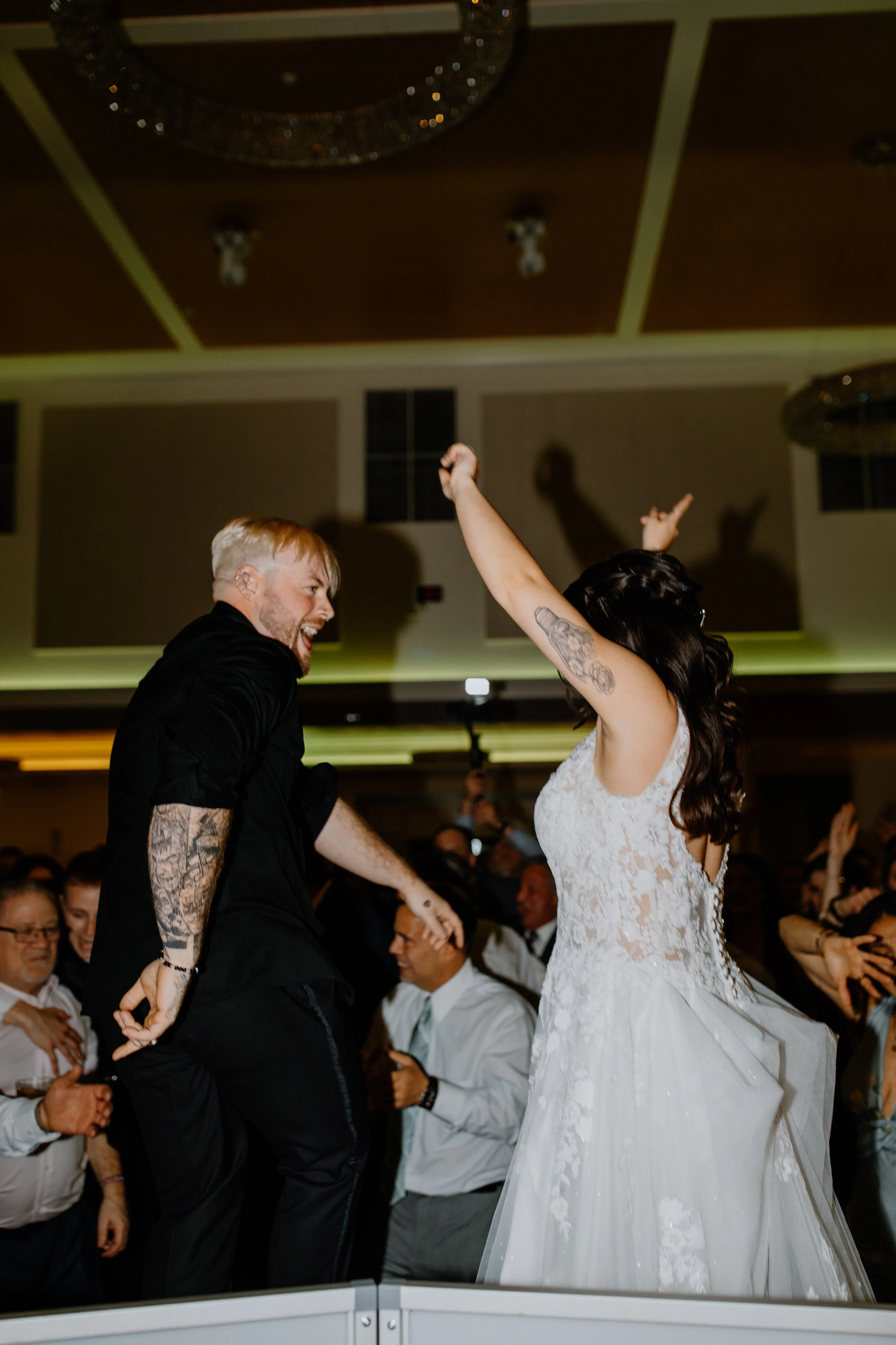 A joyful couple dancing at their wedding reception, surrounded by guests in formal attire.