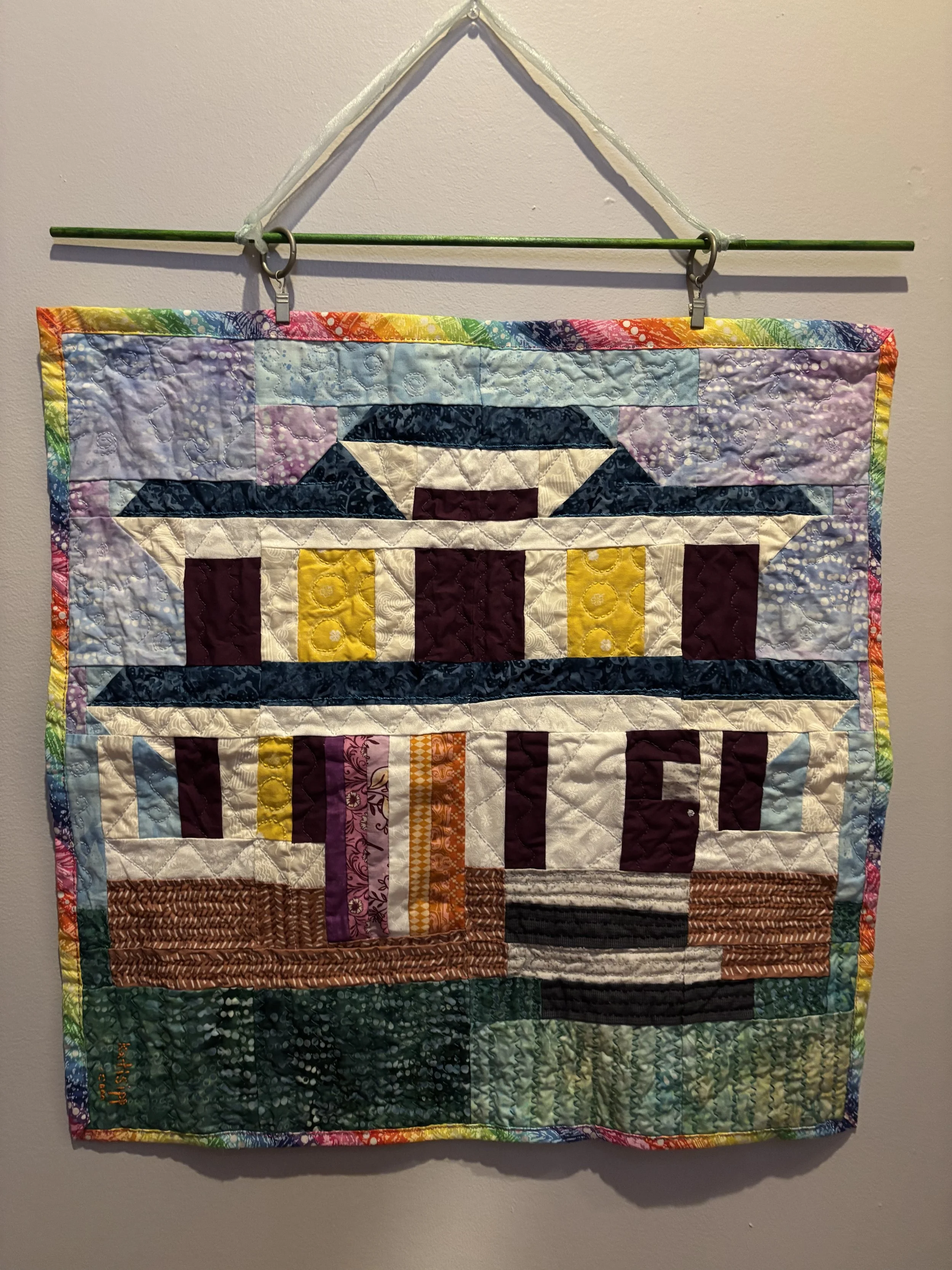 a fabric wall hanging that depicts a two story house that is displaying the lesbian pride flag