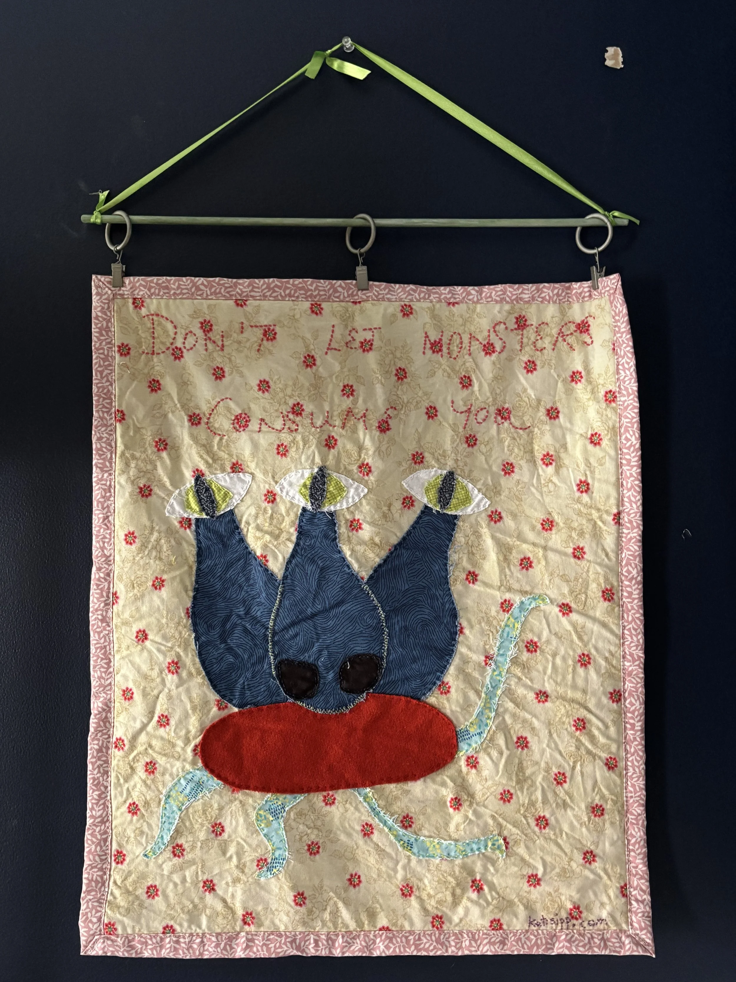 a fabric wall hanging with a picture of a 3-eyed monster, that reads "Don't let monsters consume you."