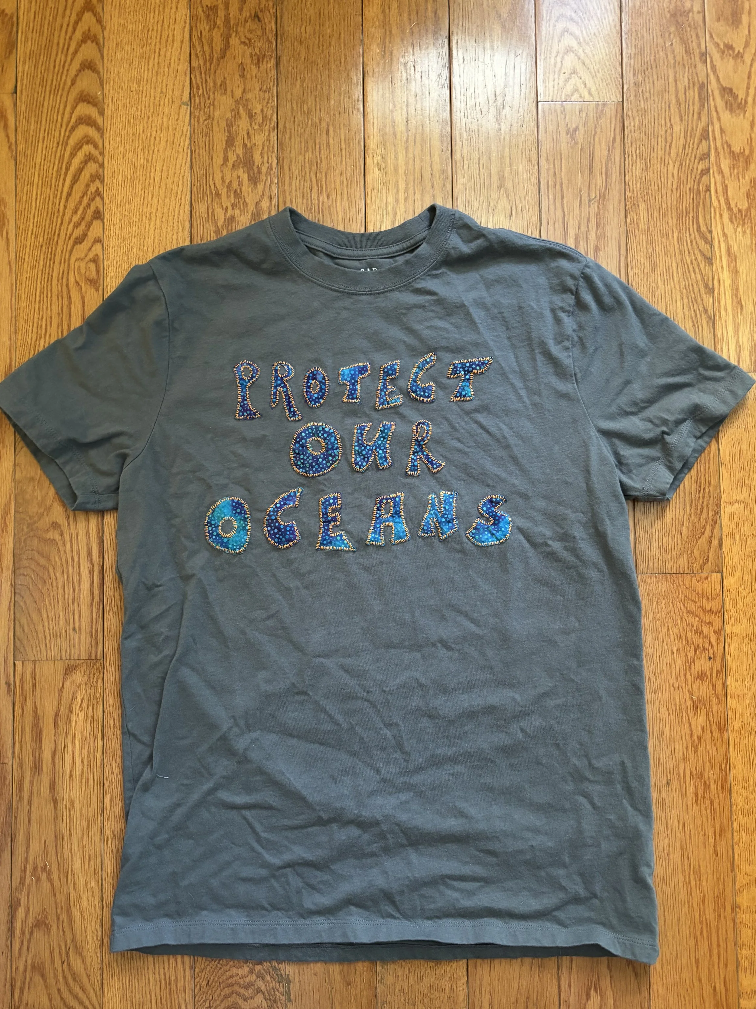 dark grey t-shirt with "Protect Our Oceans" appliqué in blue