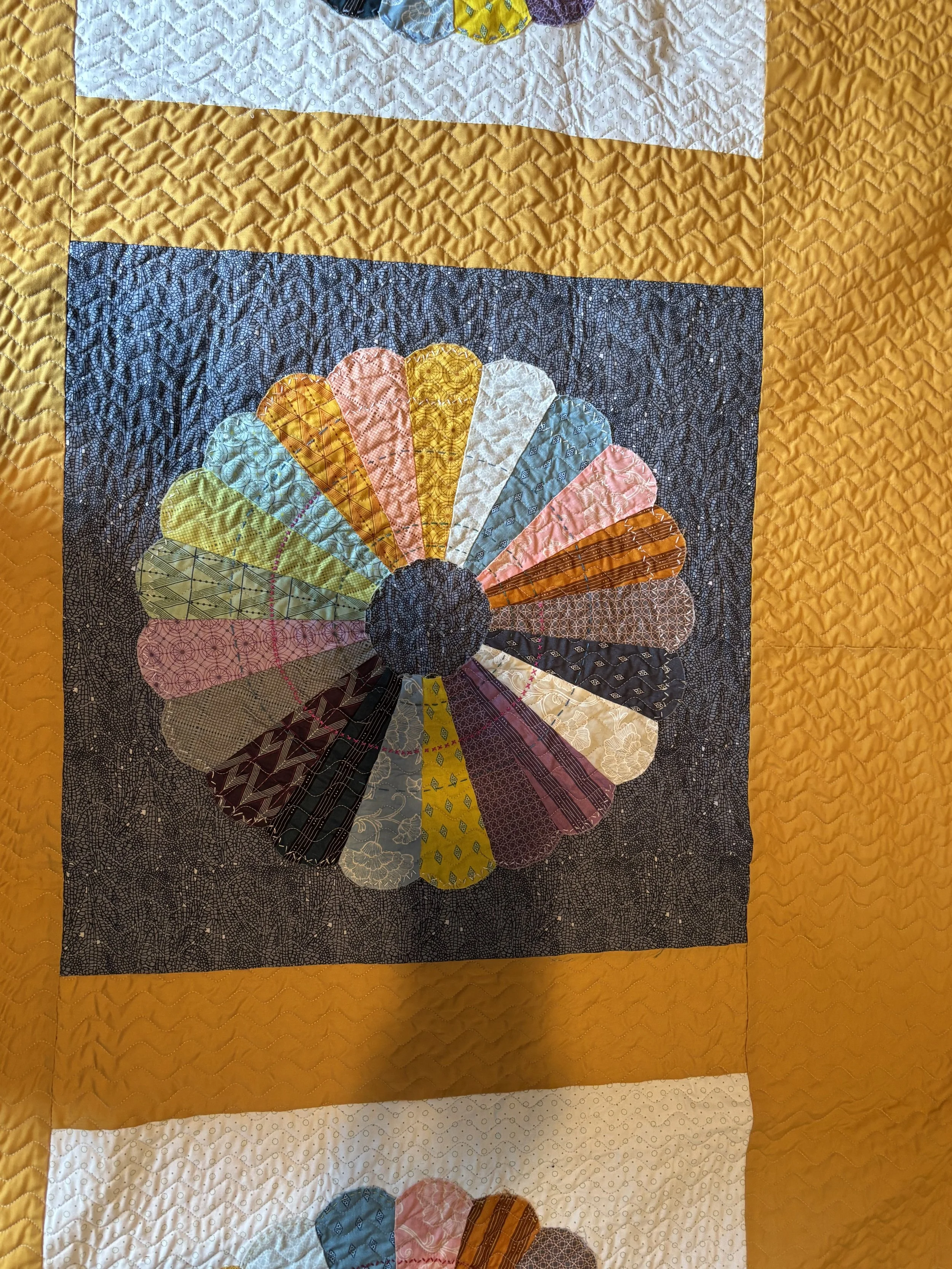 image of a type of quilt block known as a Dresden plate, featuring a circular design of many colors on a dark background