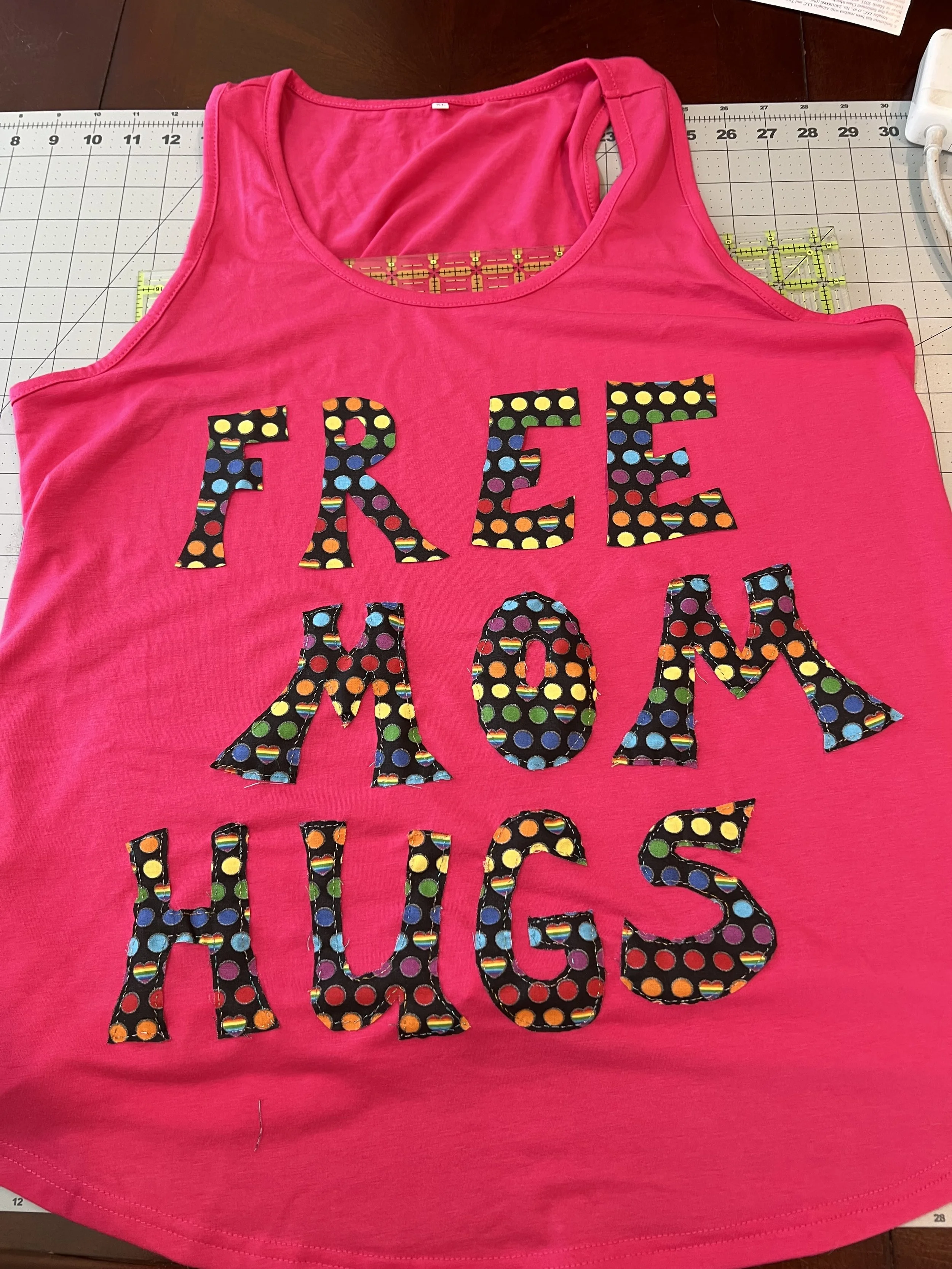 a hot pink racer back shirt with "Free Mom Hugs" embroidered with rainbow lettering