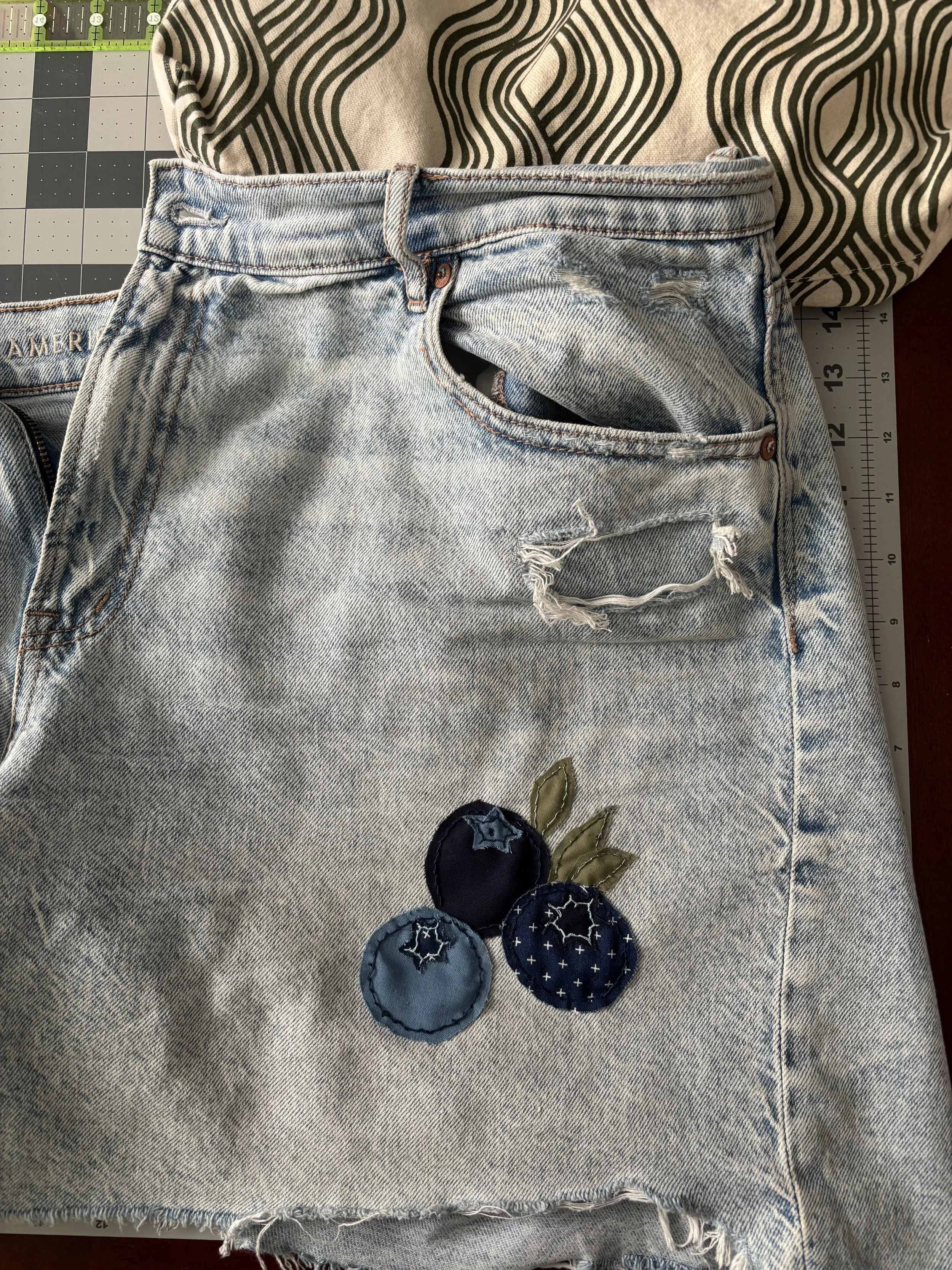 a pair of ripped denim shorts with a patch that shows 3 blueberries