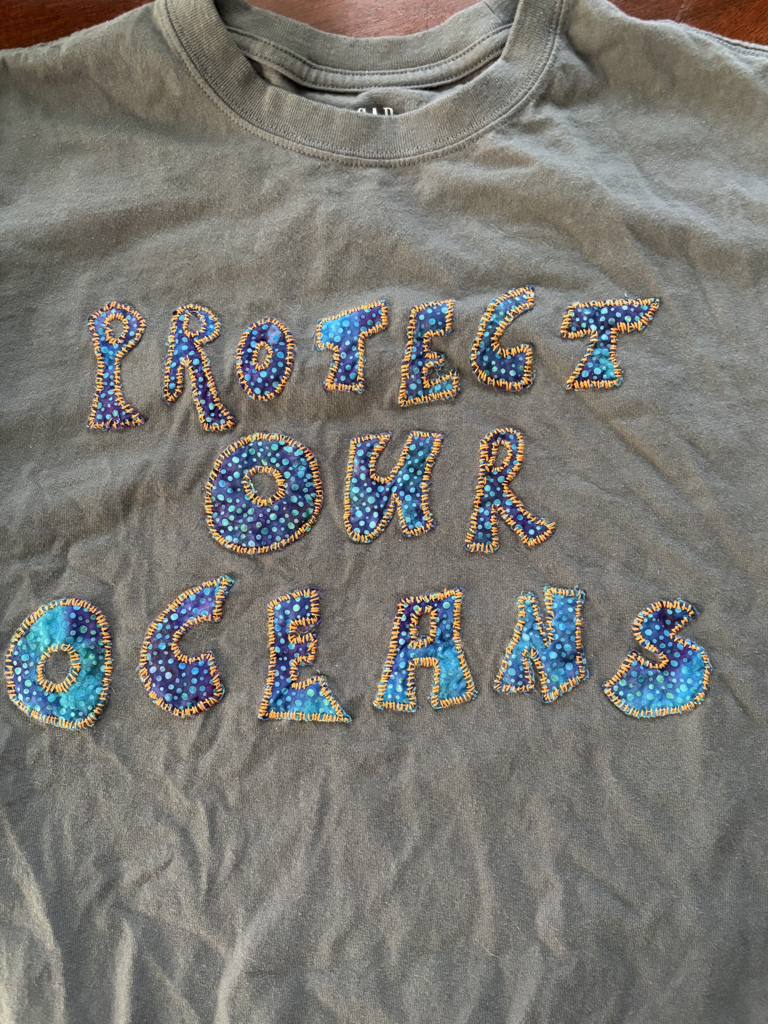 close-up detail of appliquéd "Protect Our Oceans" on dark grey t-shirt