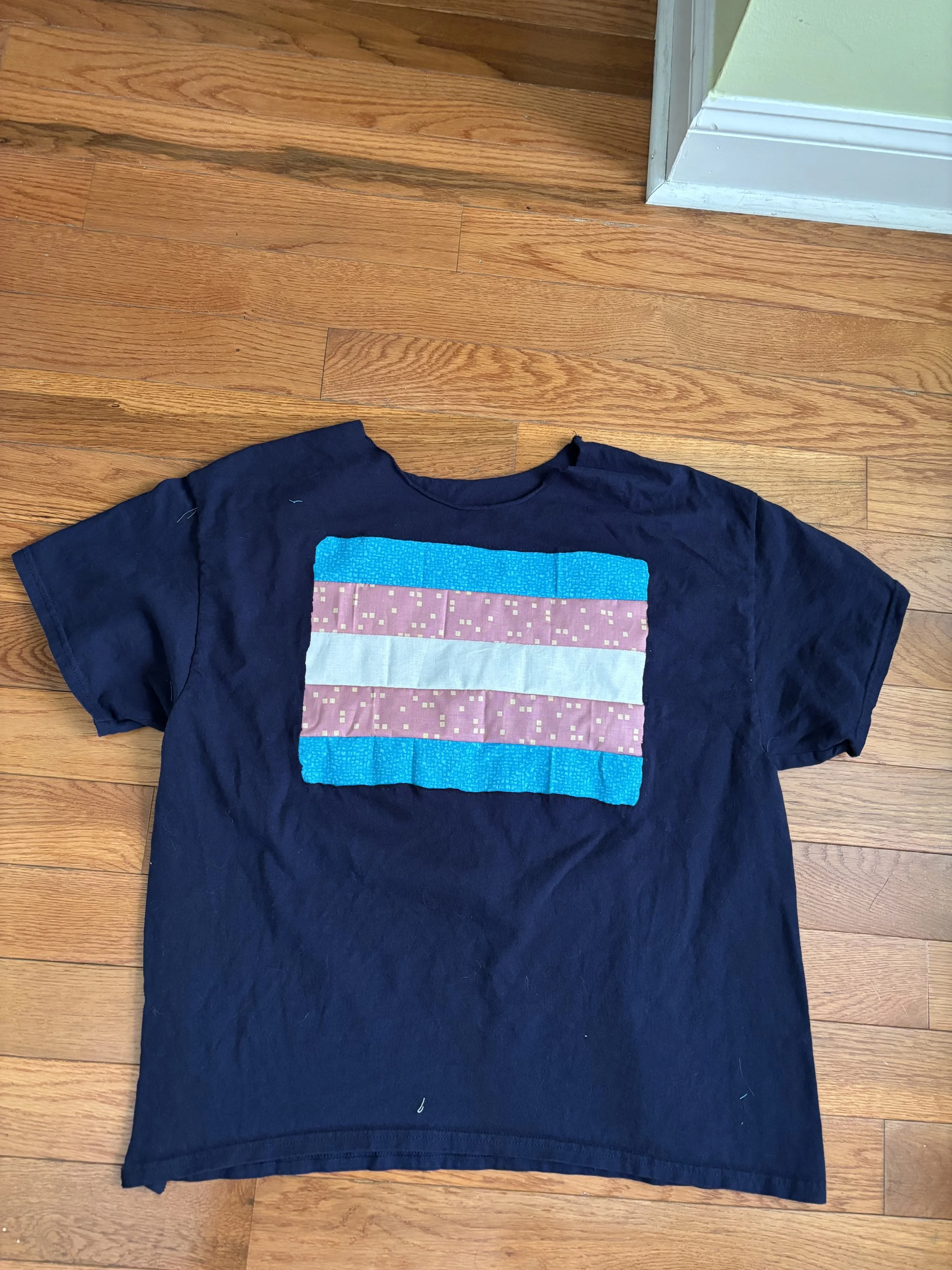 a dark blue t-shirt with a trans pride flag reverse-appliqued on it