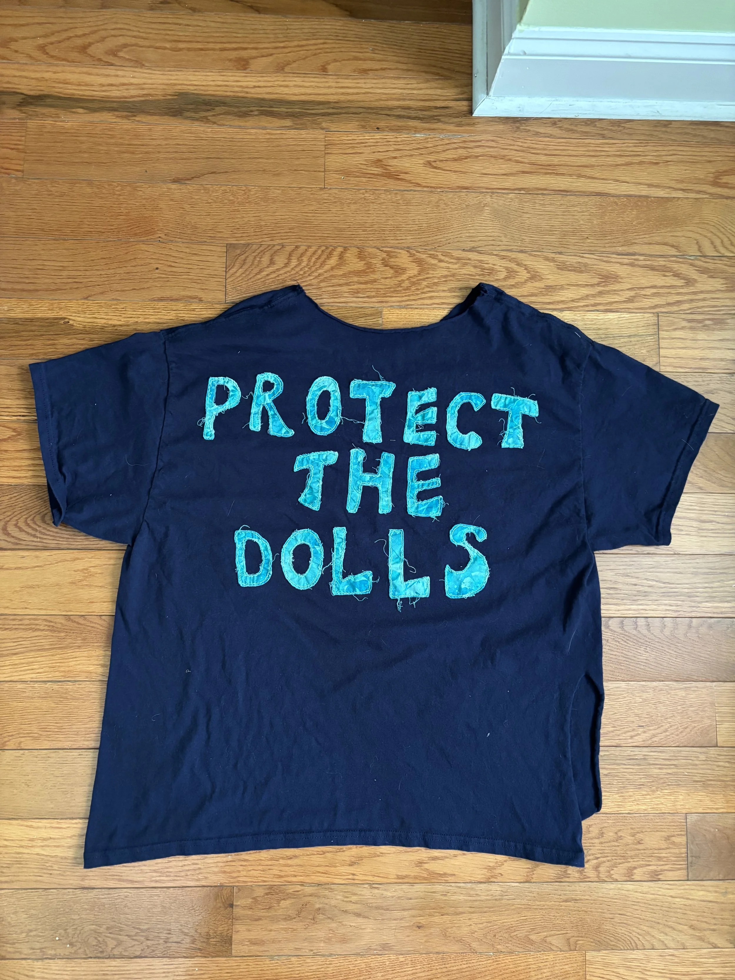 back of a dark blue t-shirt with "Protect the Dolls" appliquéd on it