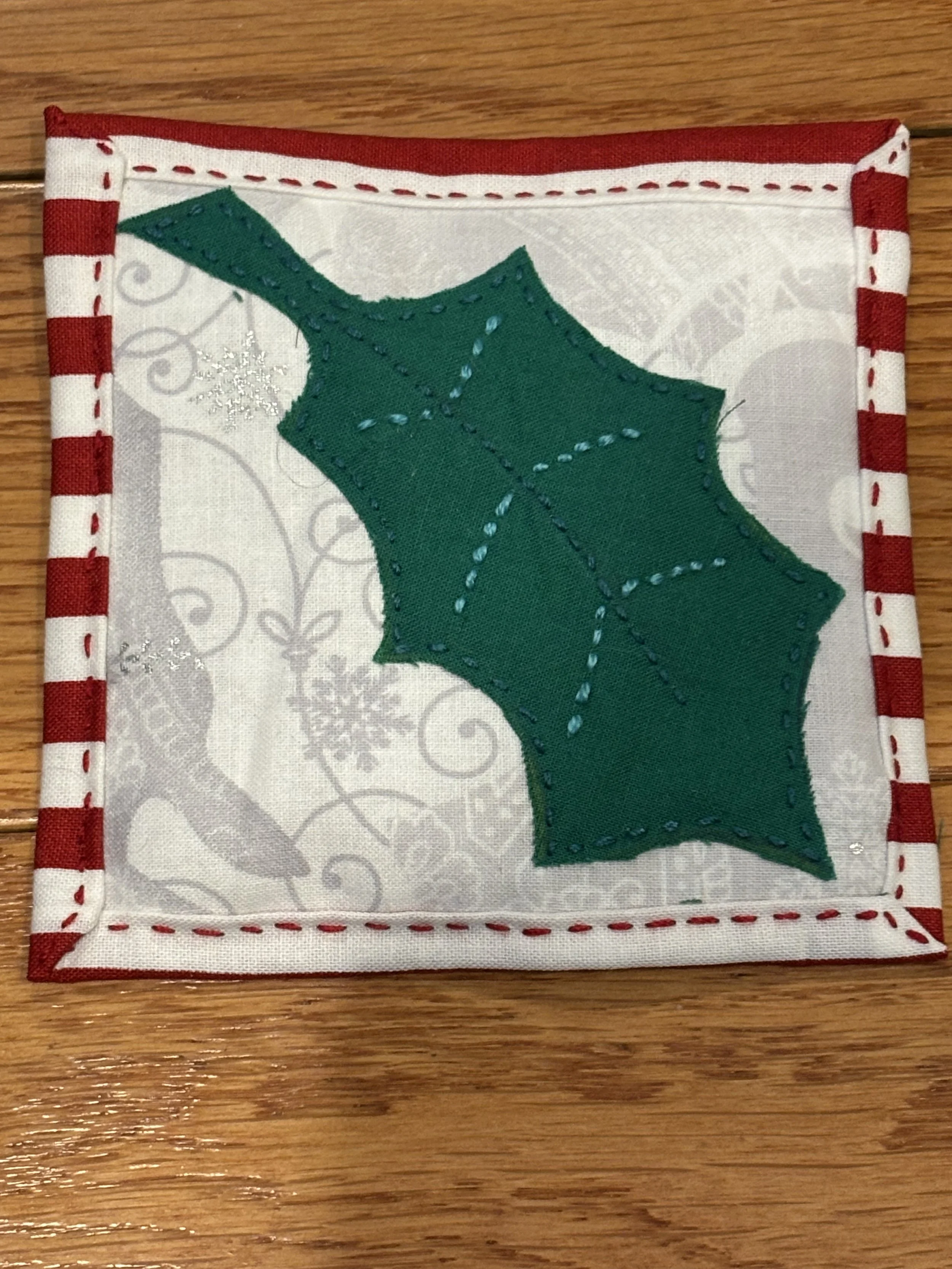 a handmade coaster with a picture of a holly leaf appliquéd on it