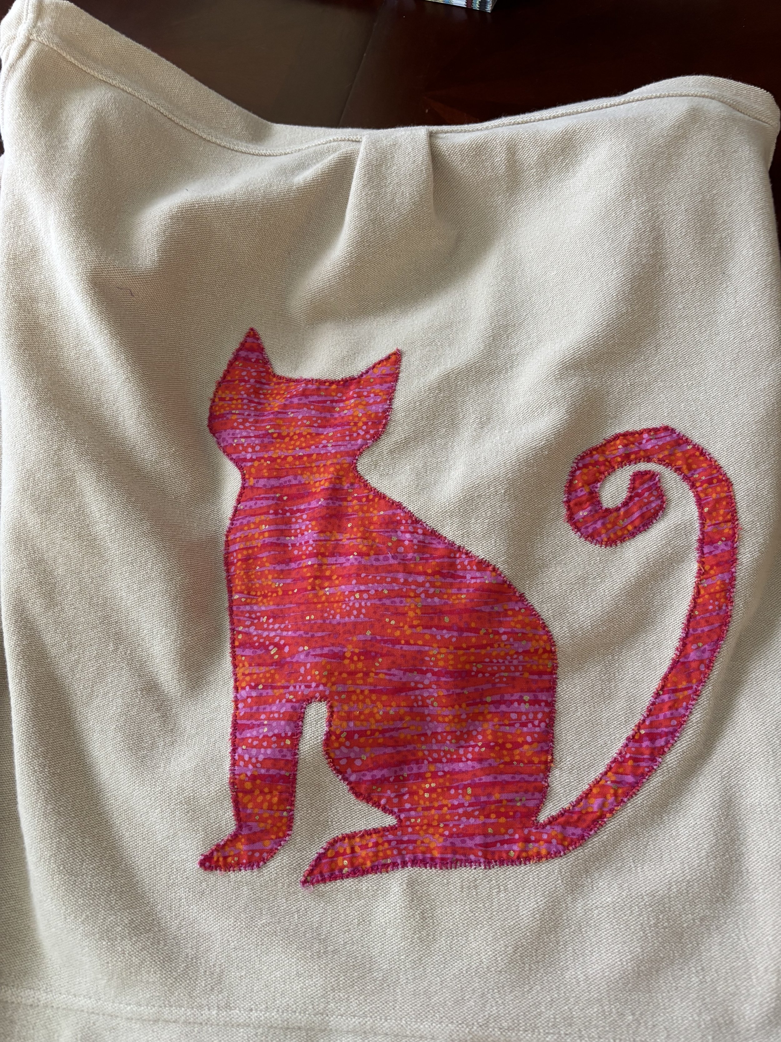 a cream button down shirt with a pink & orange cat appliquéd on the back