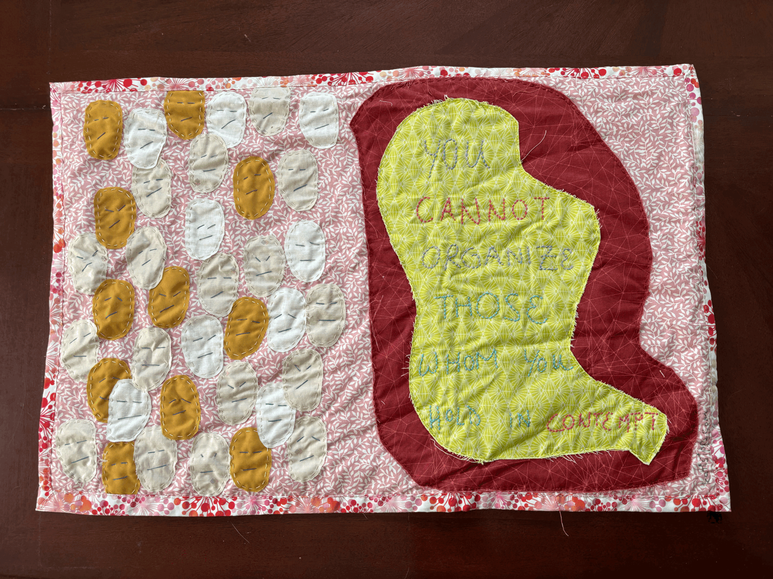 a fabric wall hanging that reads "You cannot organize those whom you hold in contempt" and depicts multiple emoji-like faces