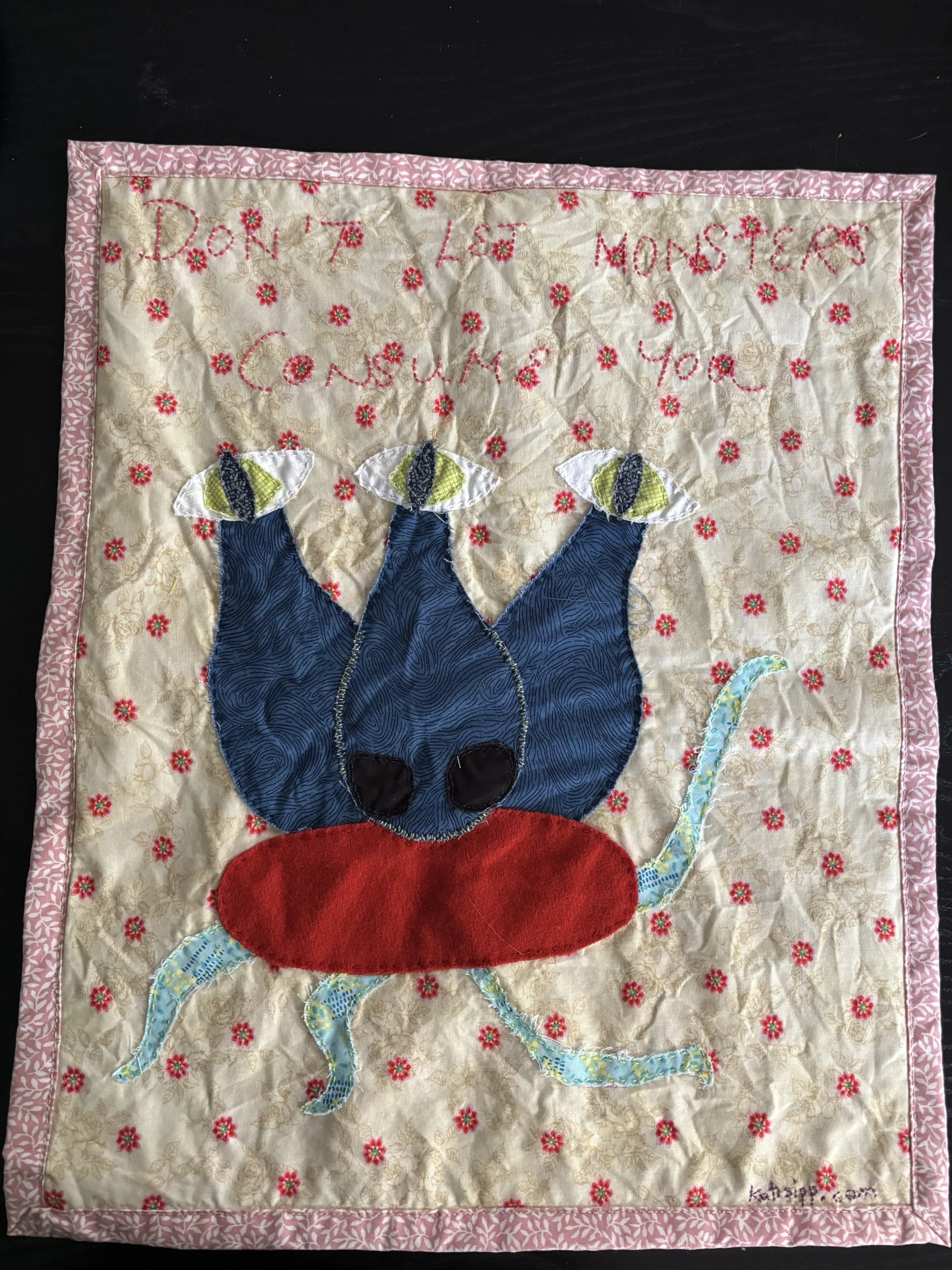 a fabric wall hanging with a picture of a 3-eyed monster, that reads "Don't let monsters consume you."