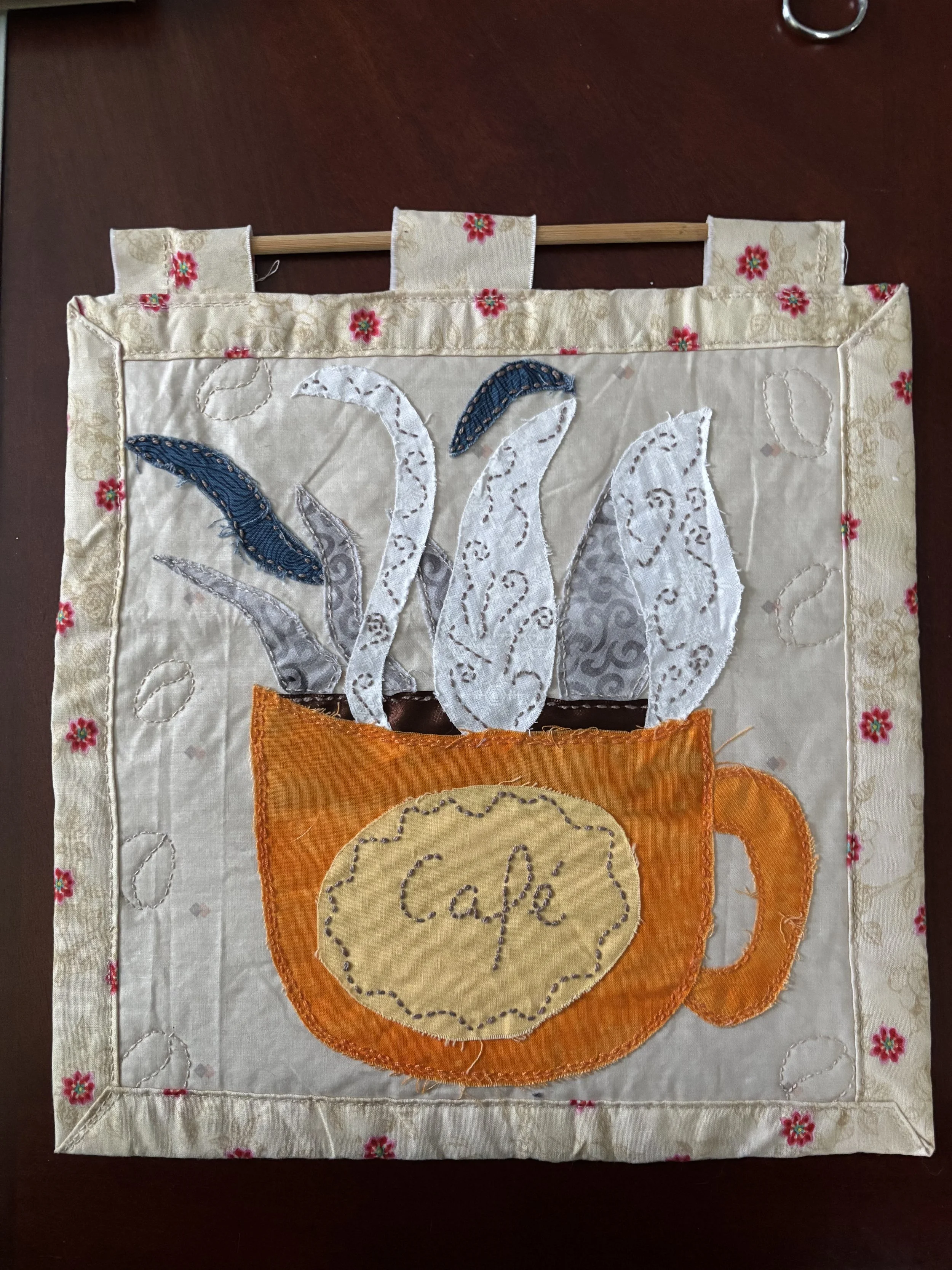 wall hanging with a coffee cup & steam appliquéd on it. The cup has a label reading "Cafe"