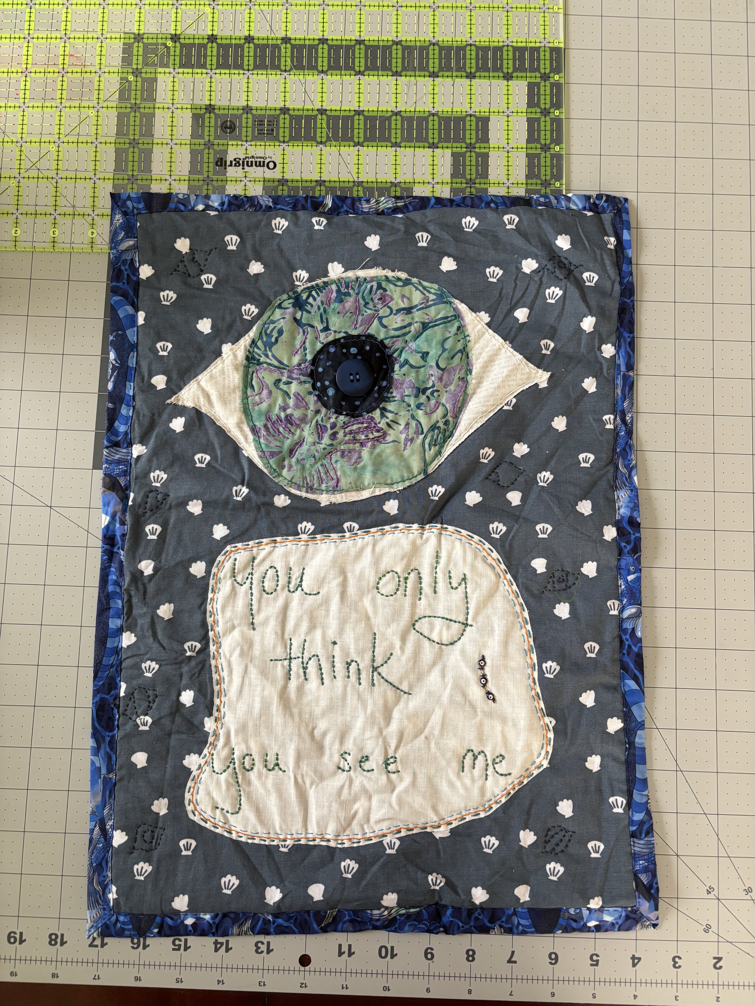 image of a fabric wall hanging that depicts a giant eyeball and the words "You only think you see me"