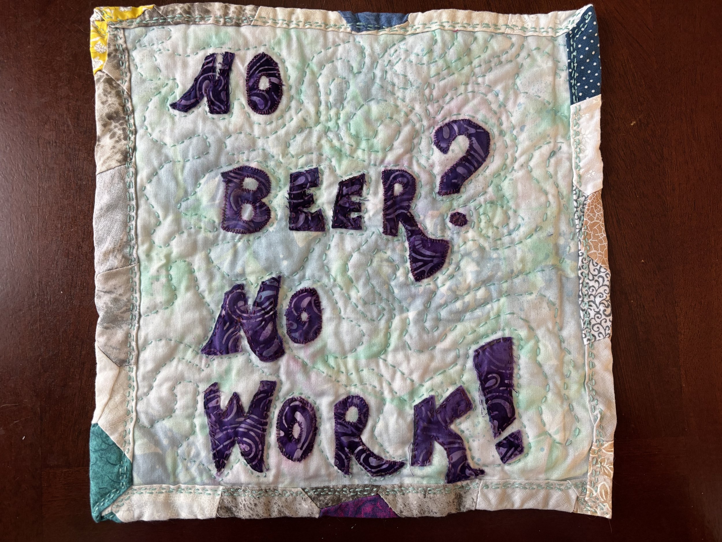 quilted wall hanging, about 12" square, reading "No Beer? No Work!" in purple batik lettering