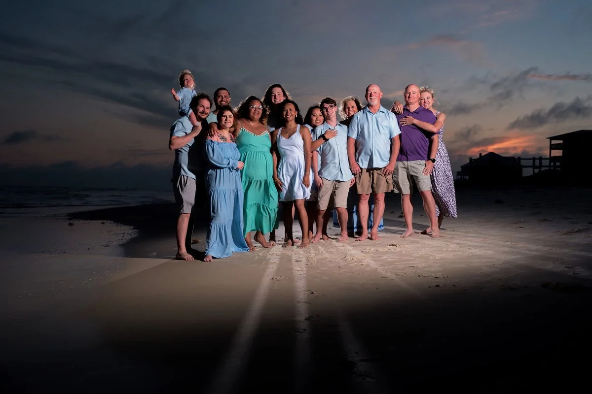 A group of people on a beach at sunset, smiling and hugging, with a darkening sky and clouds in the background in fort morgan