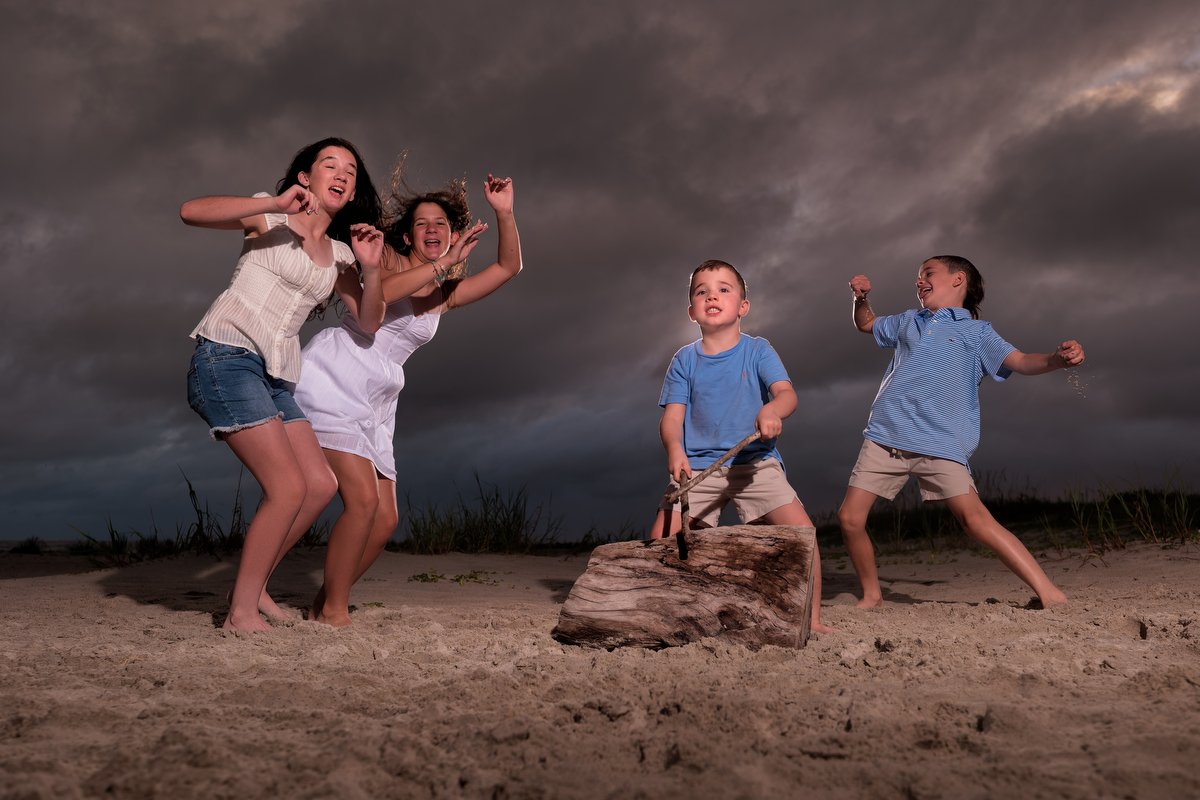 Four children on a sandy beach playing and celebrating during a stormy evening, with dark clouds in the sky at the Desoto Landing community in Dauphin Island. 