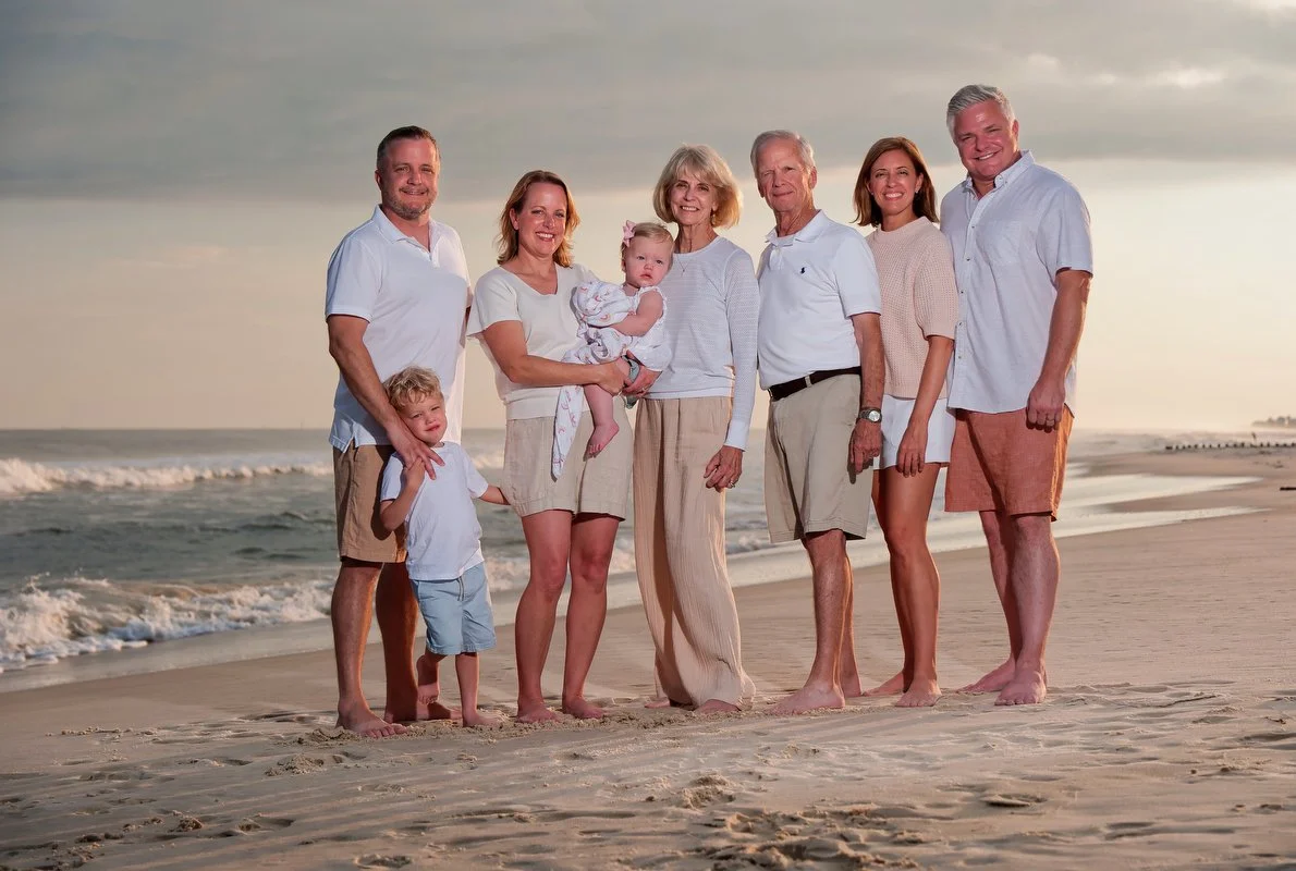 Family of eight standing on a beach at sunset, smiling at the camera.