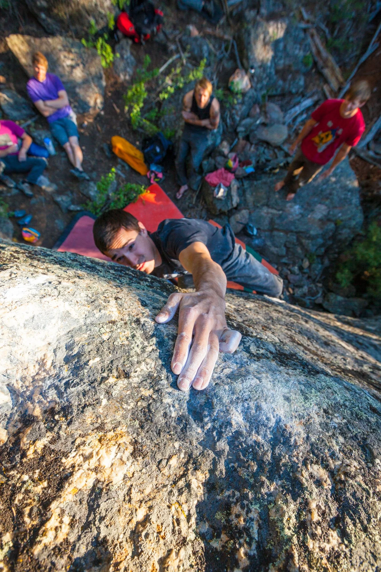 Climber scaling cliff above forested canyon with river below.