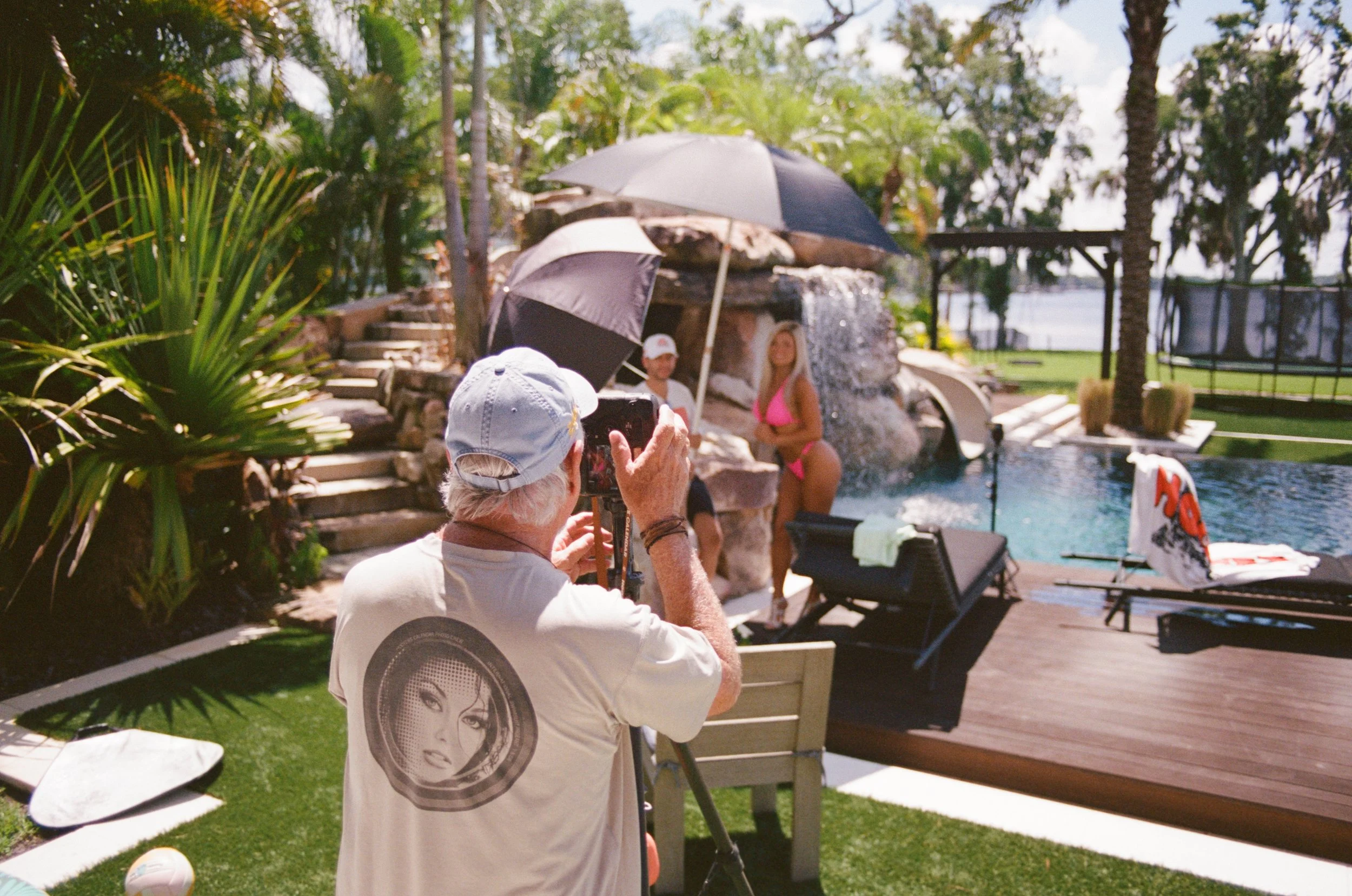 Doug taking a photo of a woman in a pink swimsuit by a pool at a backyard party.