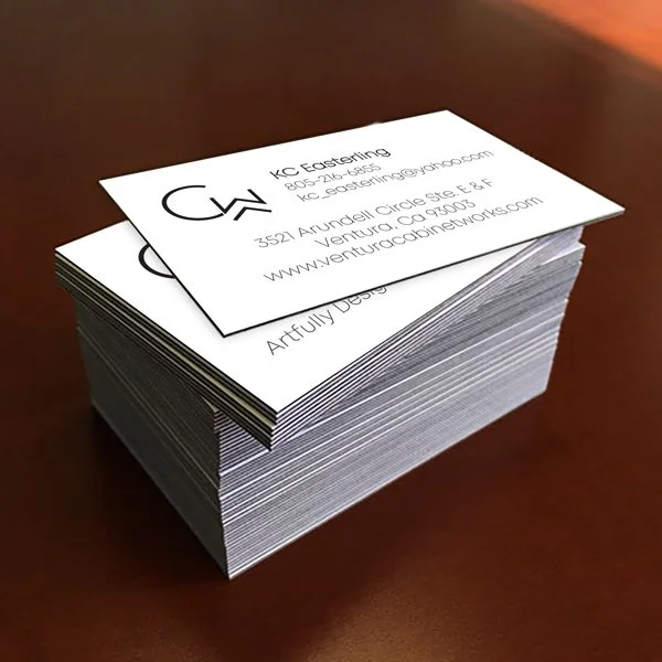 Stack of business cards on a wooden surface, with one card on top showing contact information.