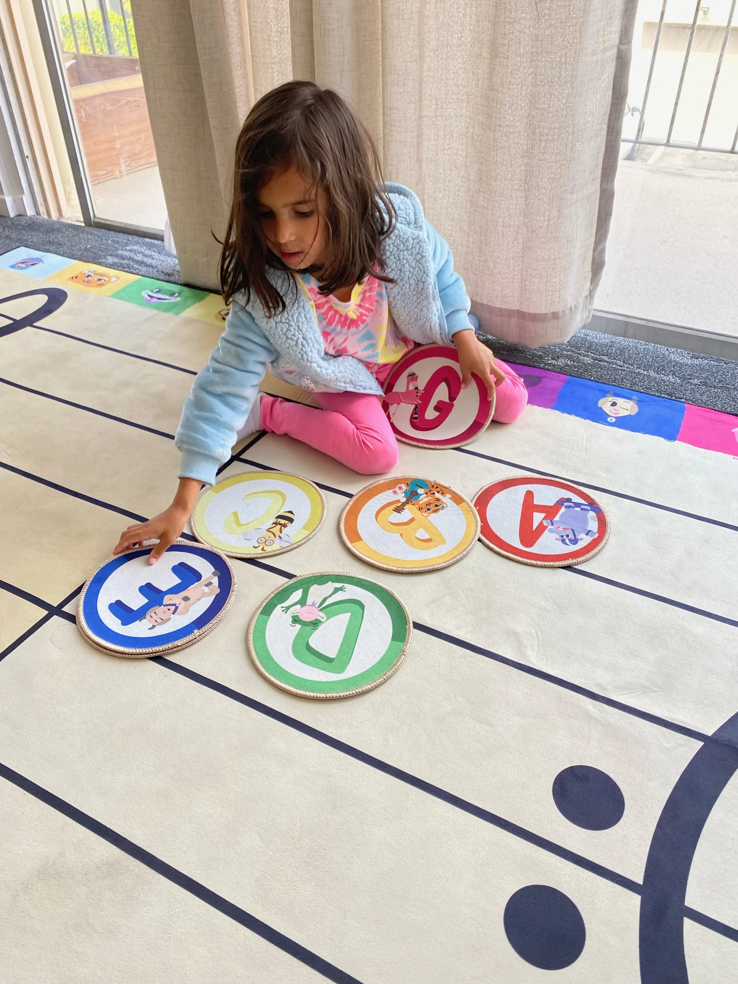 Young girl sitting on a floor with colored music note cards, arranging them in order on a large striped mat.