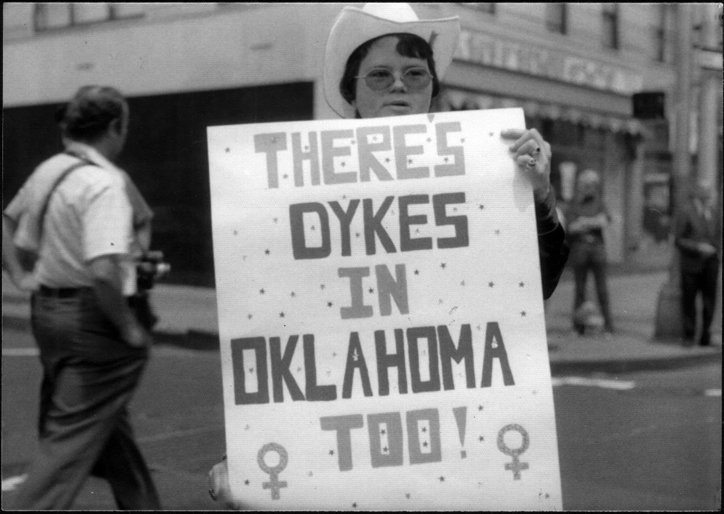 Lesbian herstory archives image of someone at a Christopher Street Liberation Day Parade with a sign "There's Dykes in Oklahoma Too"