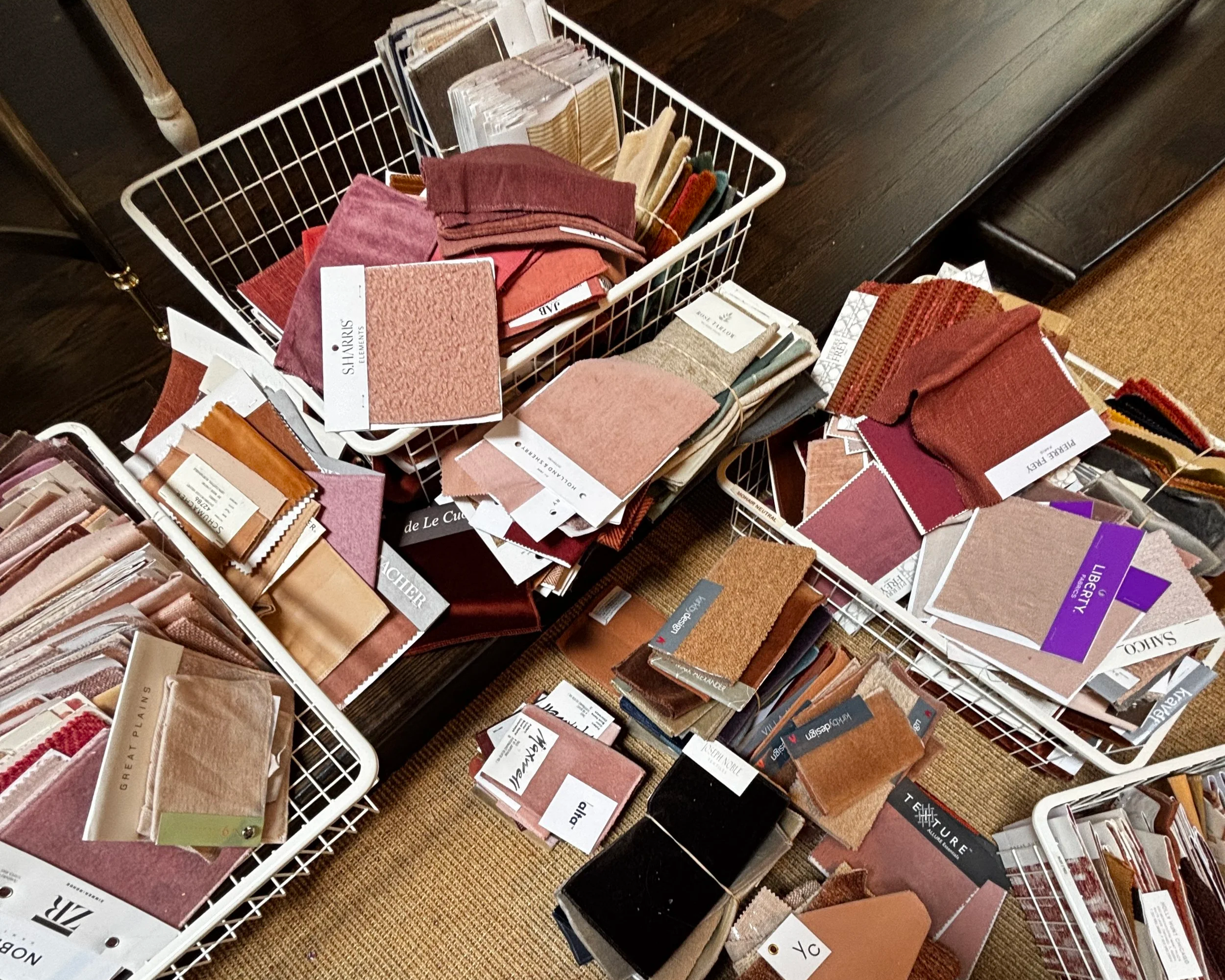 Multiple fabric sample swatches organized in white wire baskets on a dark wooden surface.