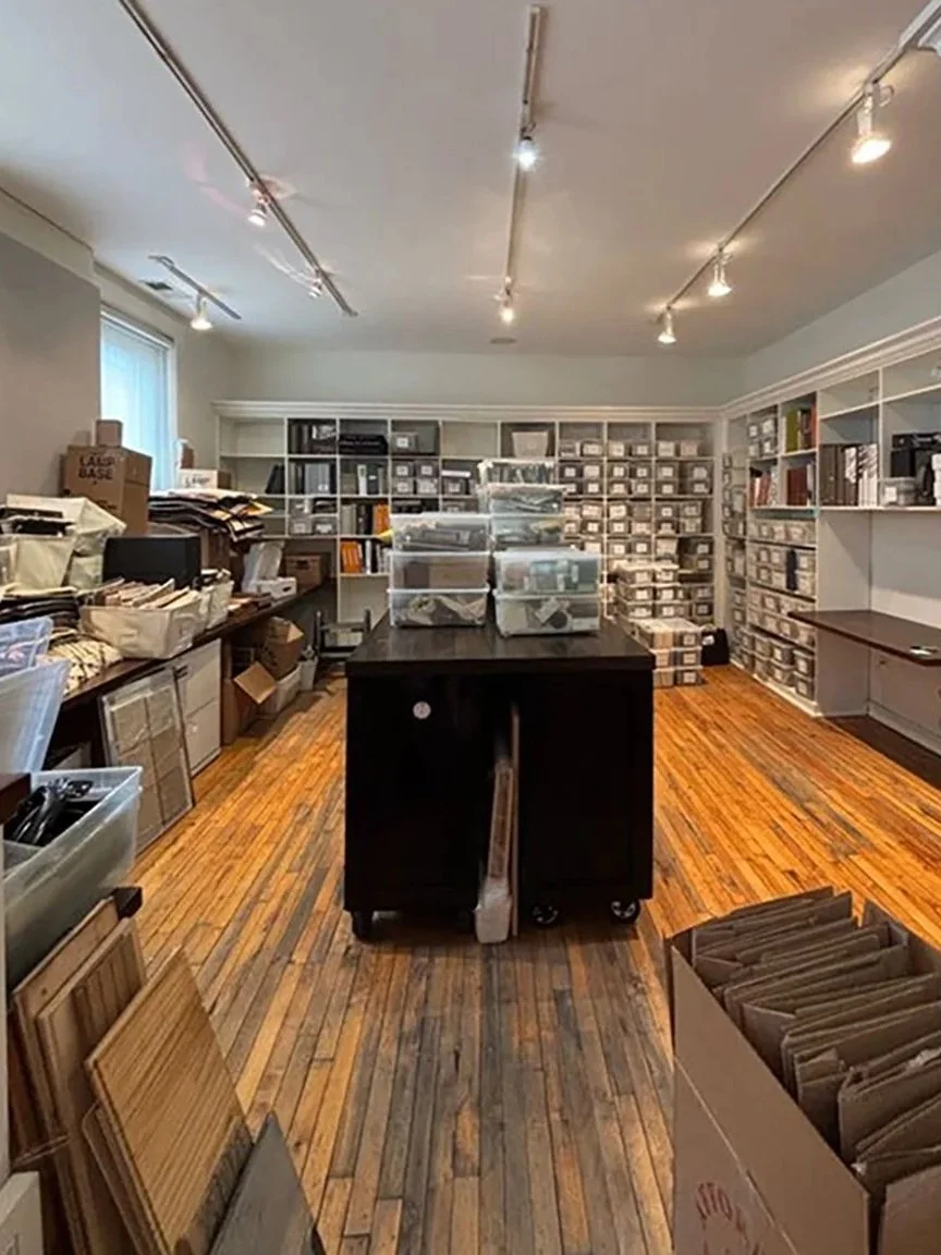 A room filled with organized storage bins and shelves, a central black table with stacks of boxes, and a hardwood floor.