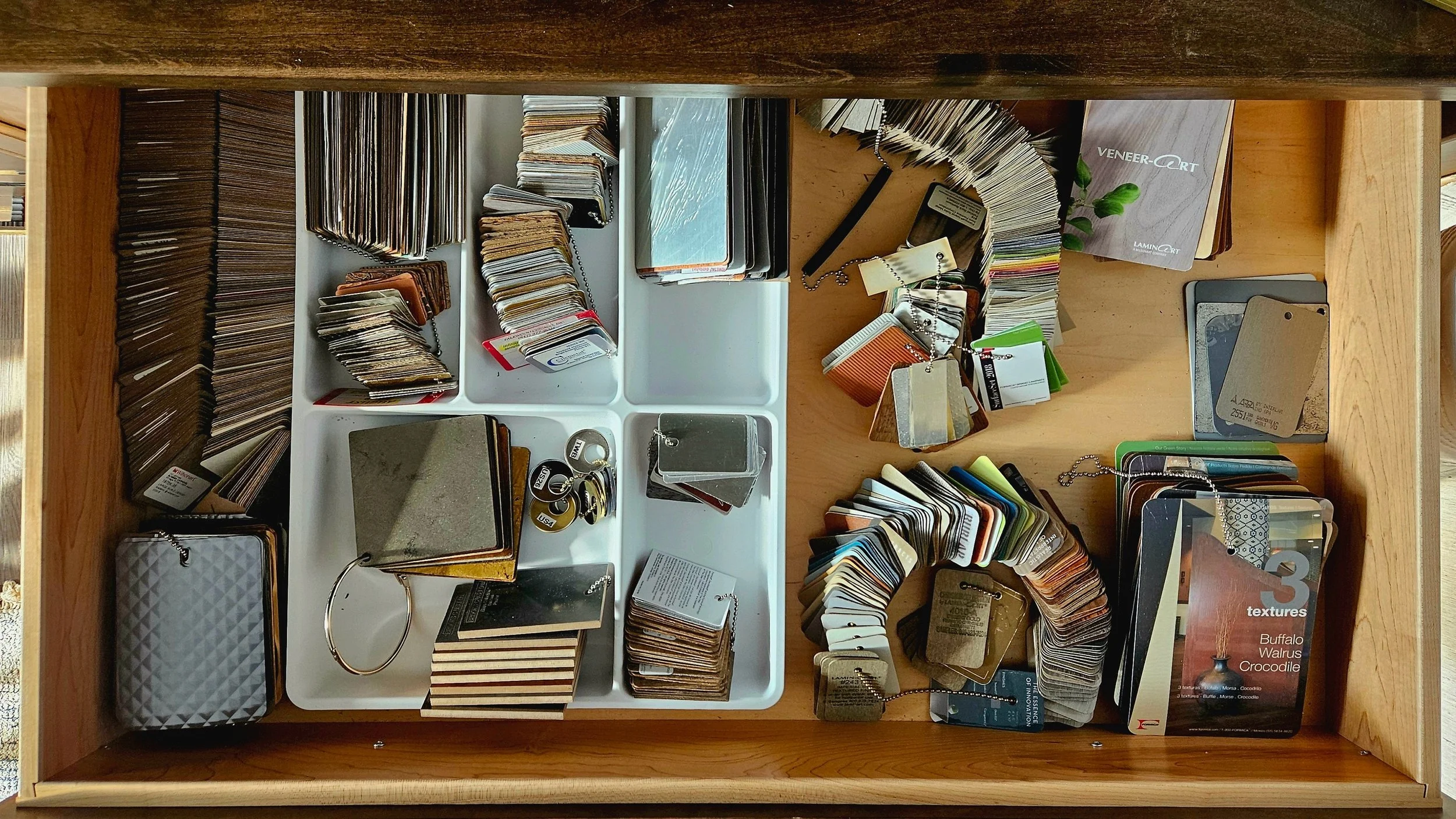 A wooden drawer with various color and texture samples, metal key rings, and small samples of materials.
