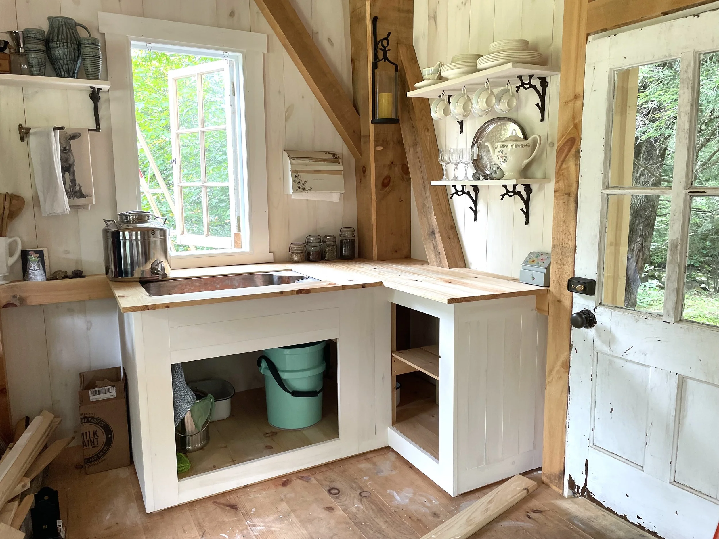 The completed kitchen cabinet, minus its curtains. Plumbing is a 5 gallon bucket.