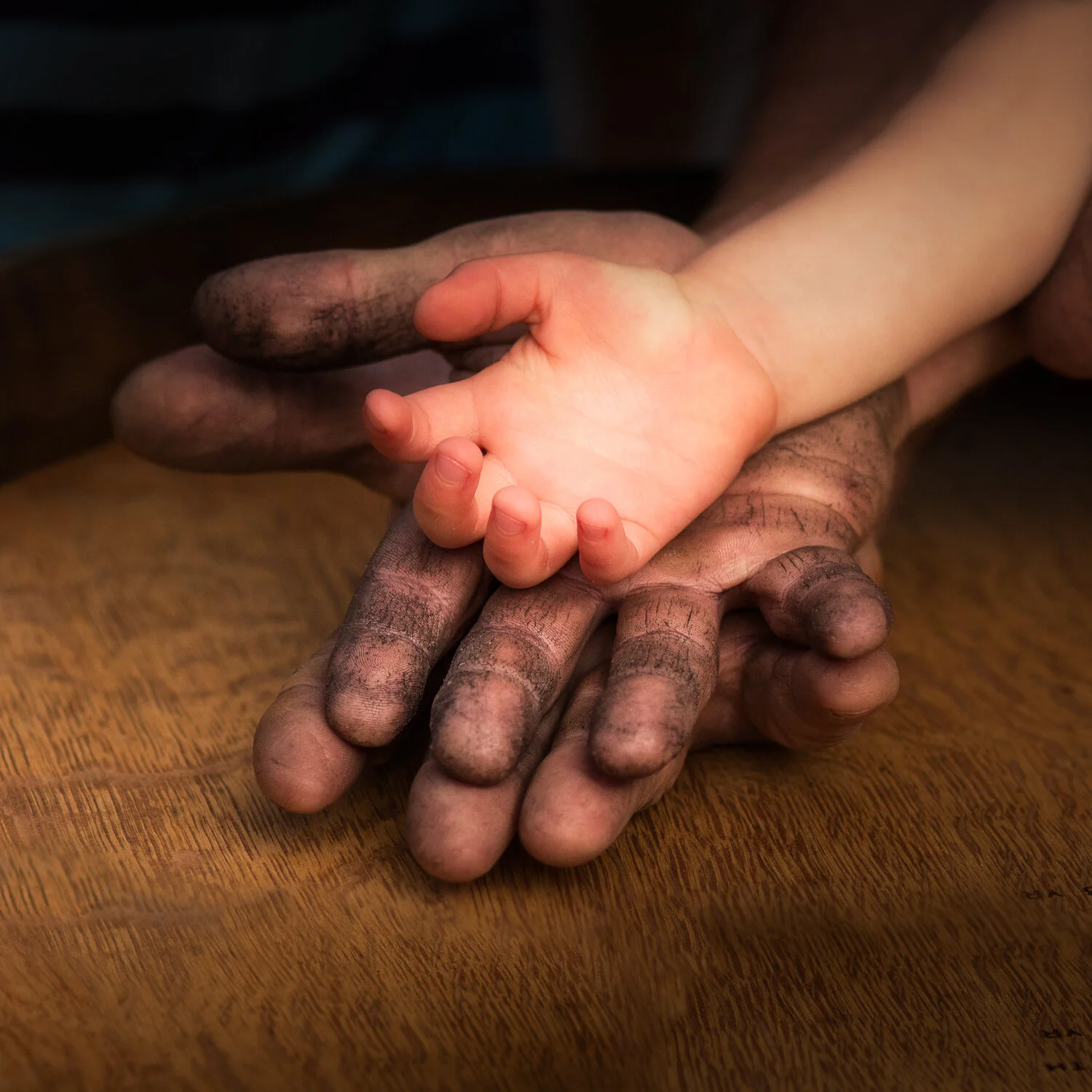 Child's hand resting on adult's dirt-covered hands on wine barrel