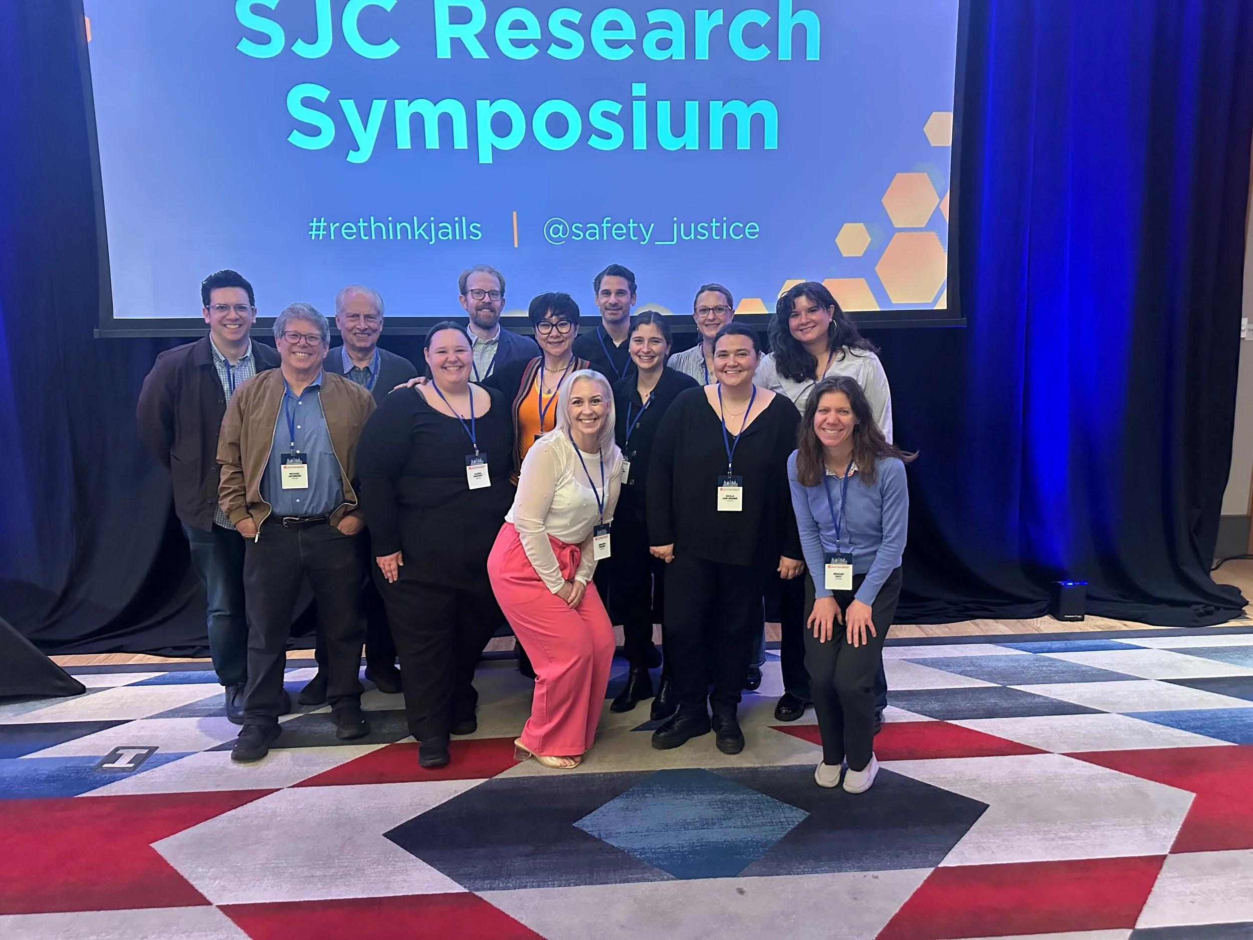 CUNY ISLG staff members smile together in front of a screen that says "SJC Research Symposium"