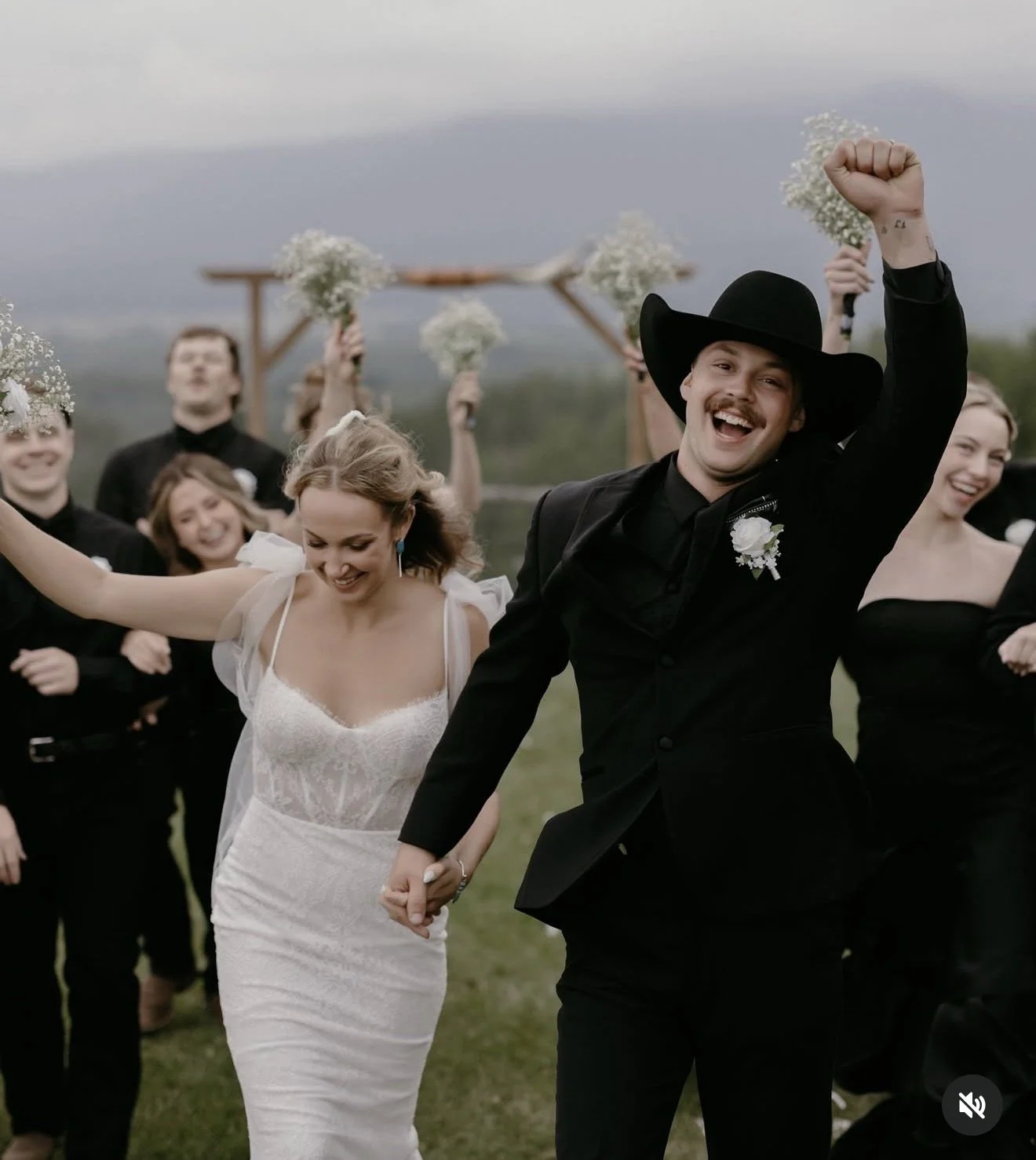 country wedding for real bride wearing her Chantilly lace wedding gown with bows and her husband in a black suit with a black cowboy hat on their farm