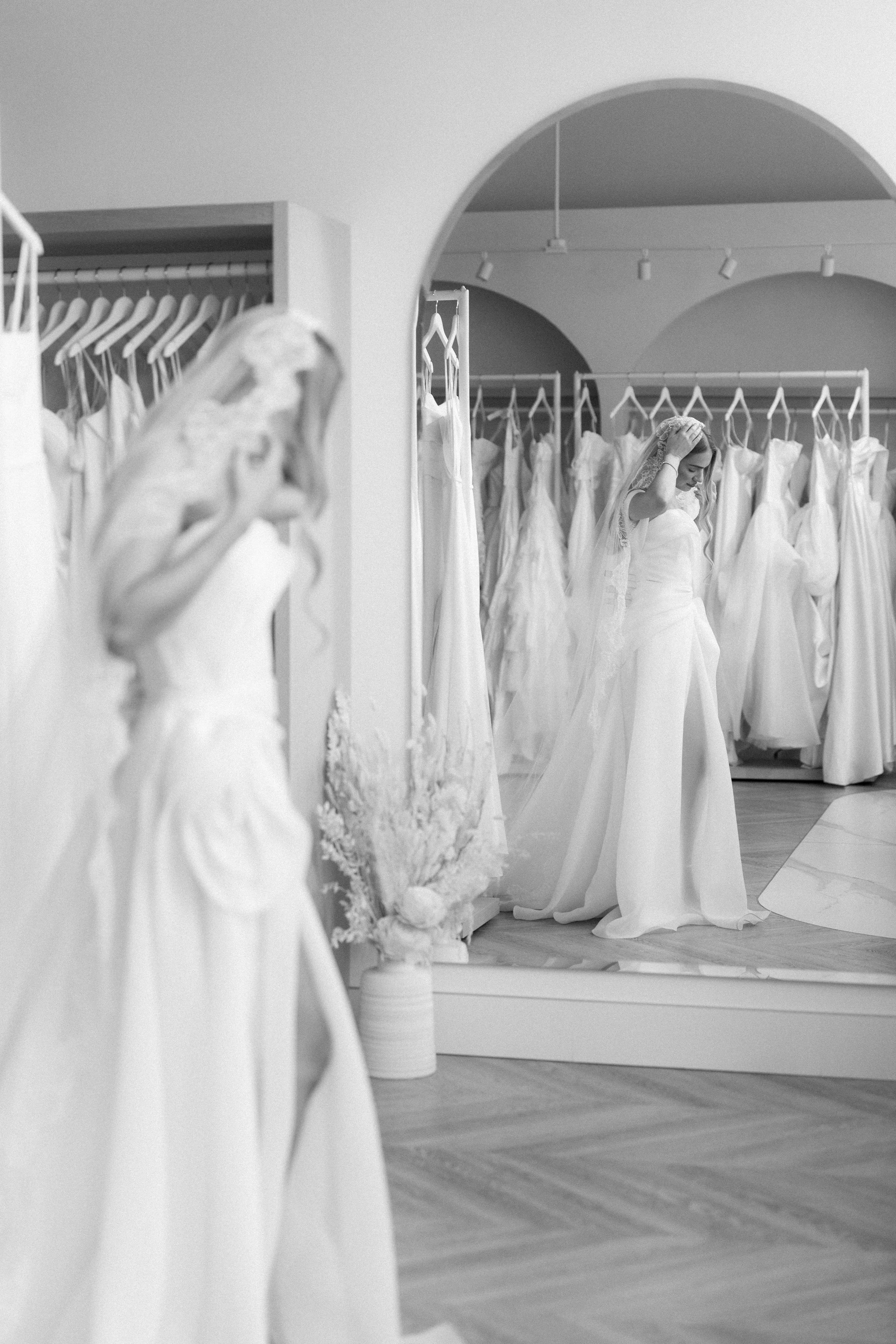 A beautiful bride in a designer wedding gown and chantilly lace veil, walking around The Bridal Boutique in search of her perfect dress. Beautiful dresses and florals in the background and you can see the brides refection in the mirror