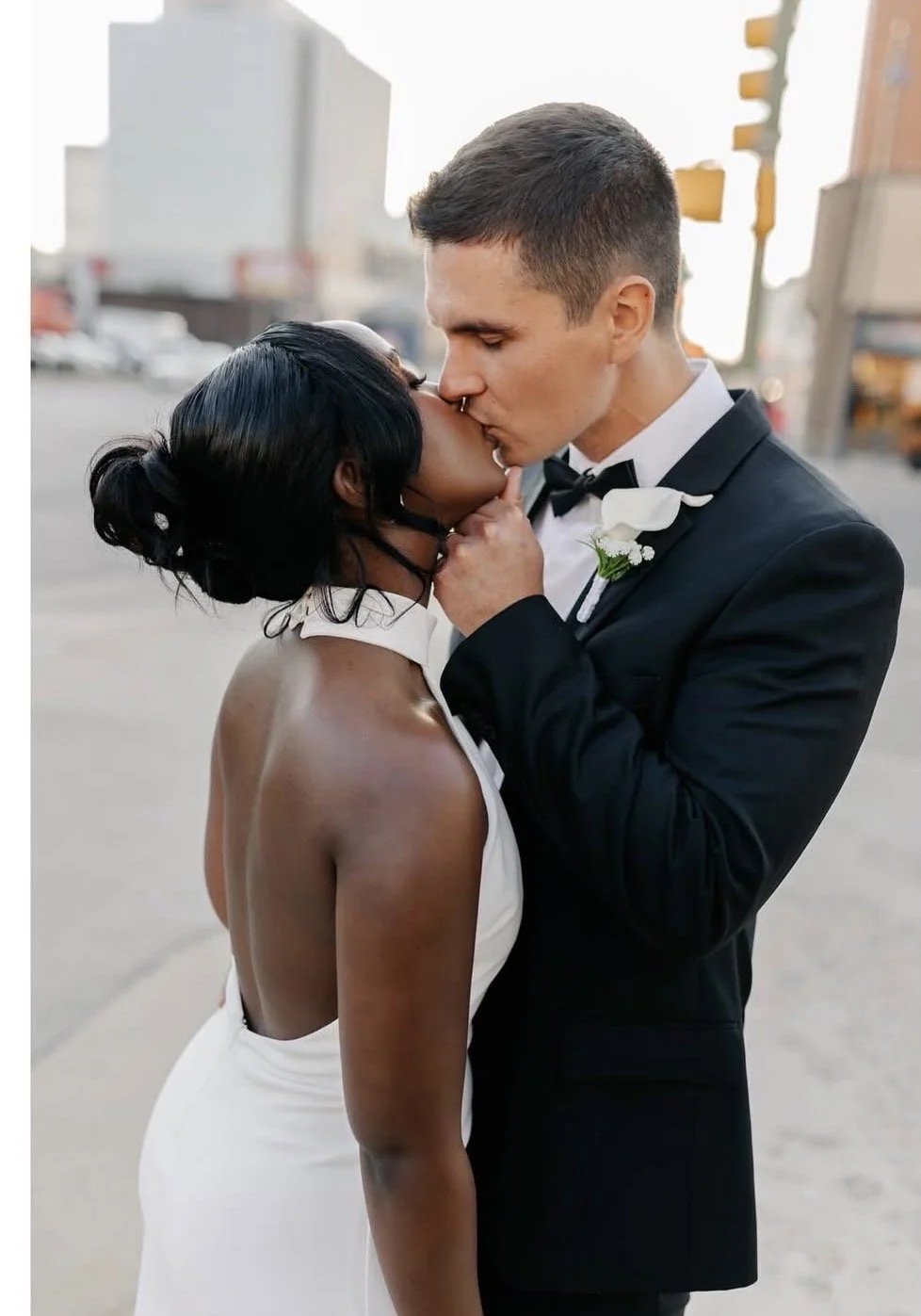 real bride who found her dress at The Bridal Boutique sharing a kiss with her husband. Her dress is a low back halter