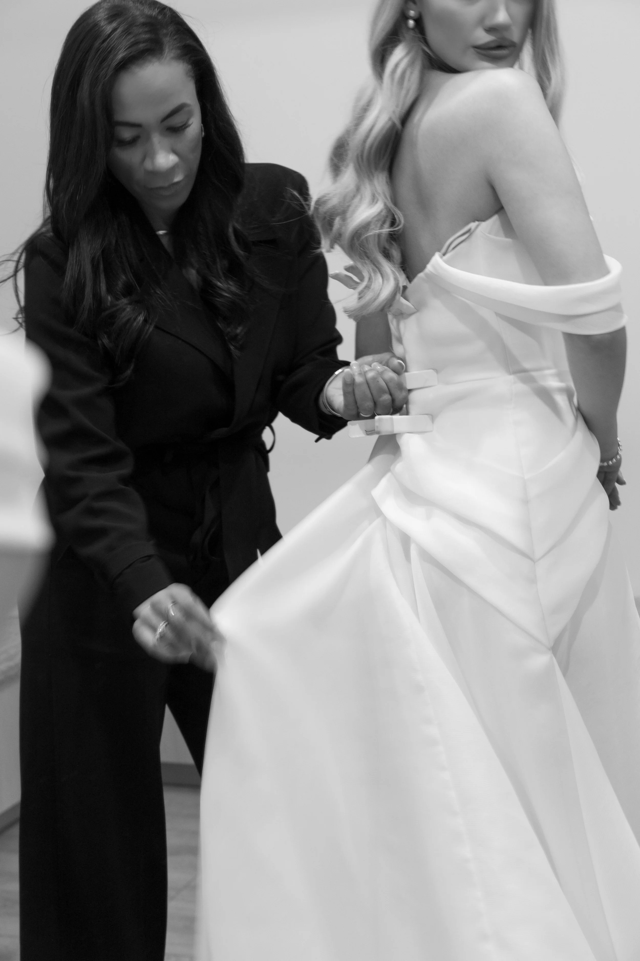 A woman in a black outfit helping a bride with her wedding dress, black and white photo.