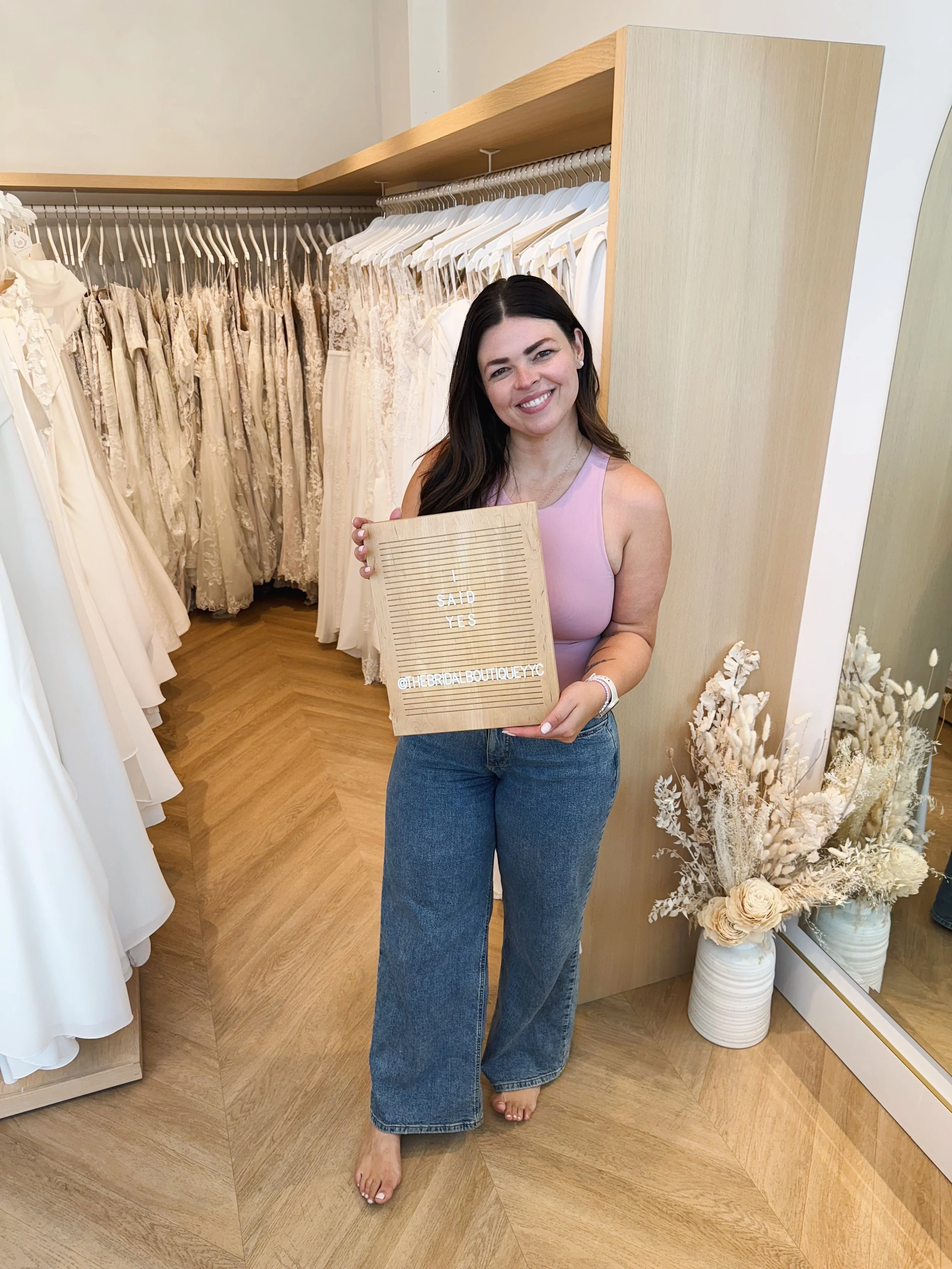 A well know bride, Josie Balka holding a "I said yes to the dress" sign at The Bridal Boutique
