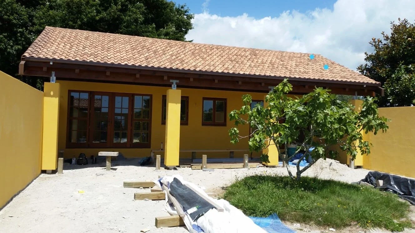 Painted by Europlast Systems in Tauranga, Bay of Plenty. House with yellow exterior walls, brown window frames, a tile roof, a tree in the yard, and ongoing construction work.